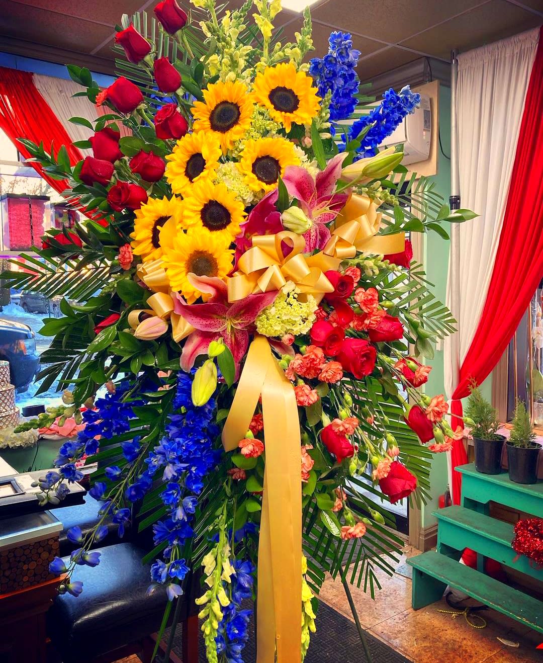 Large standing floral spray with sunflowers, red roses, and blue flowers
