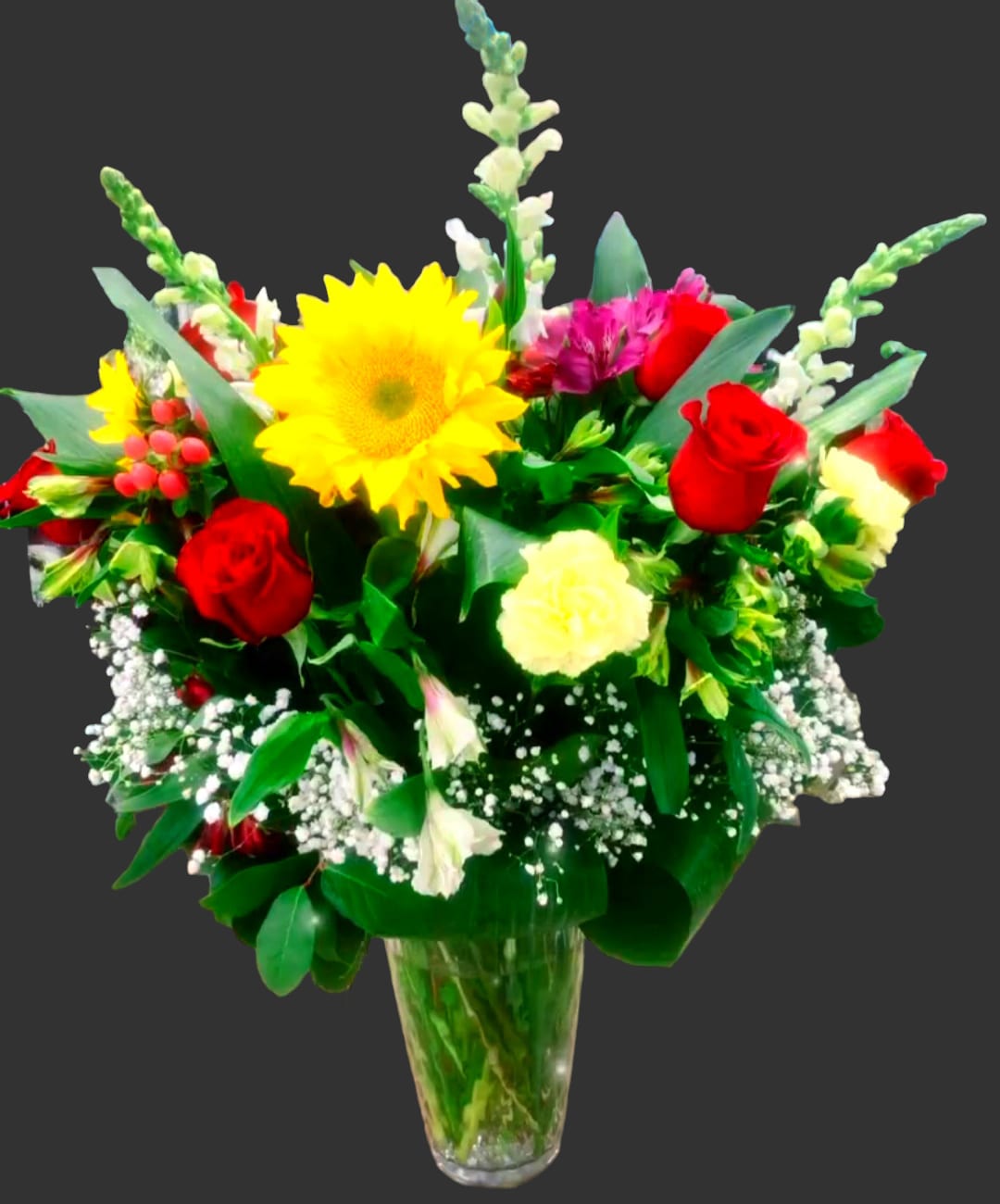 Mixed bouquet of red roses, yellow sunflower, and pink flowers in a glass vase