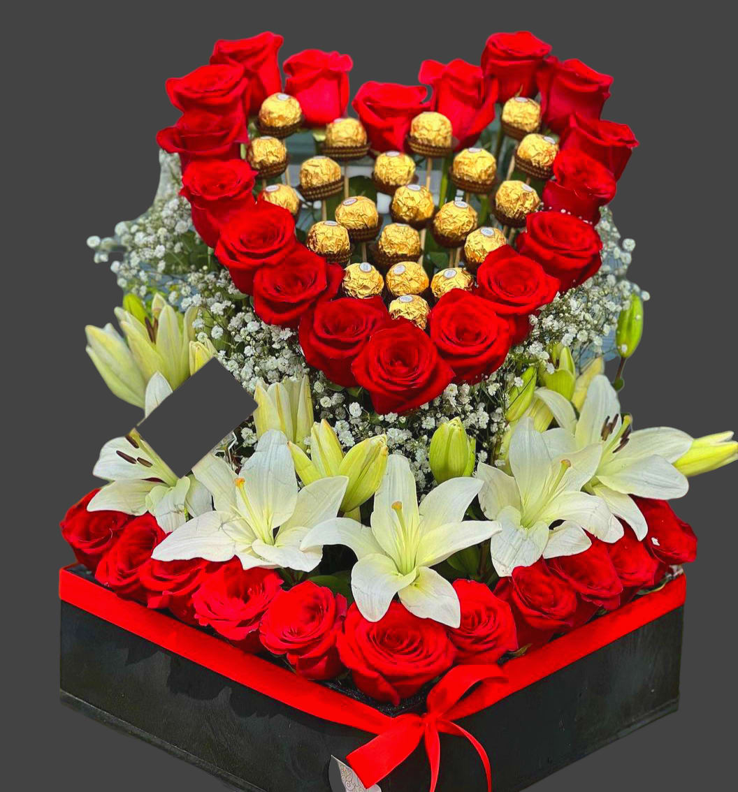 Heart-shaped rose and chocolate arrangement with white lilies in a black box