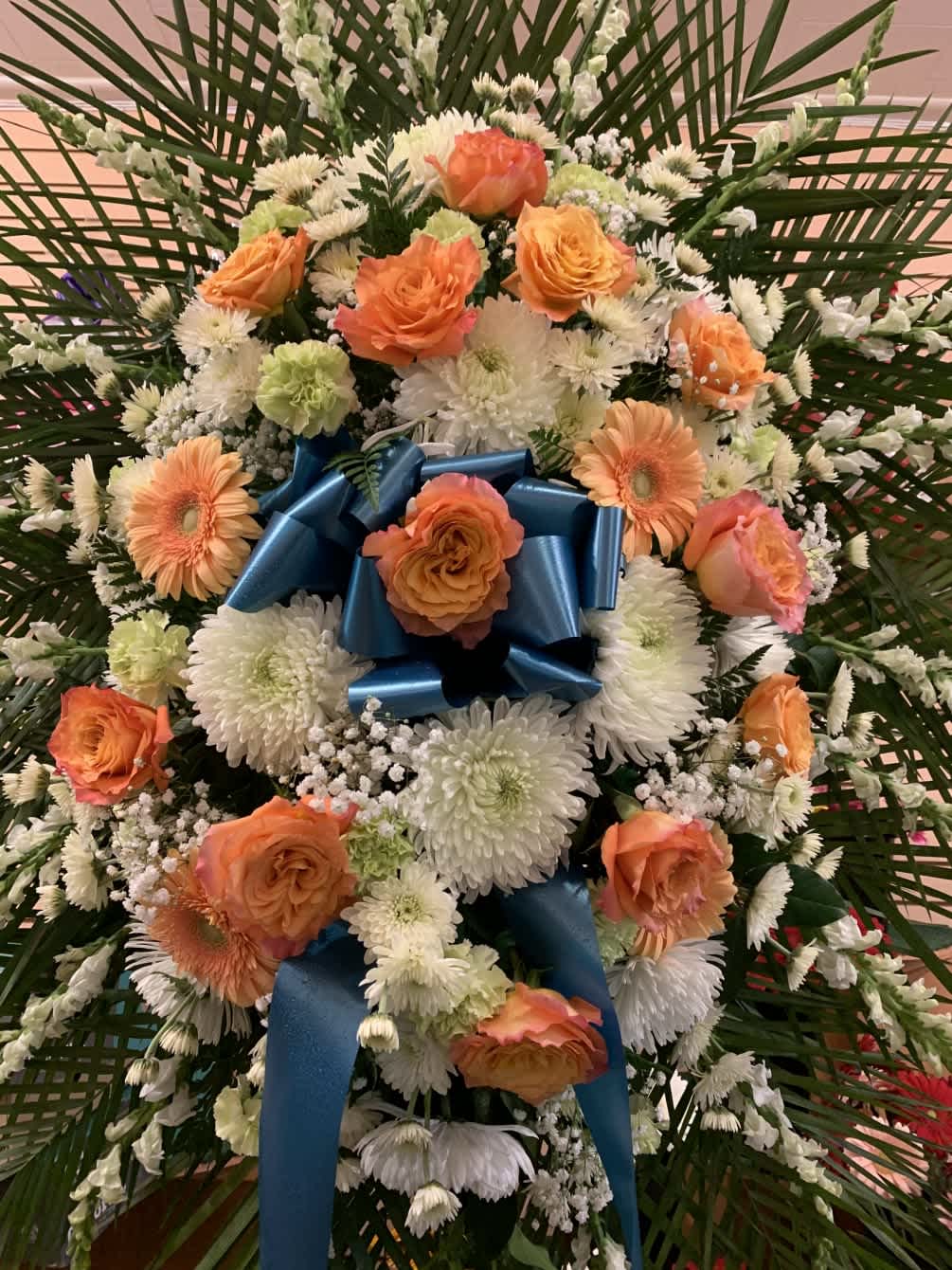 Large floral standing spray with orange roses and white daisies, finished with a blue ribbon