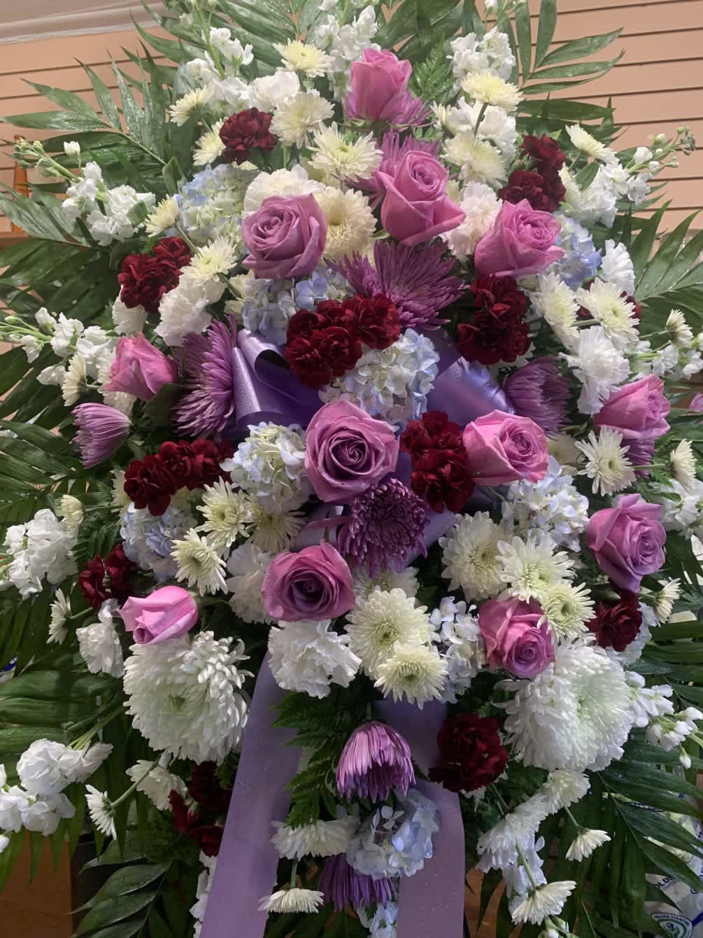 Large floral spray with pink roses, white chrysanthemums, and purple ribbon