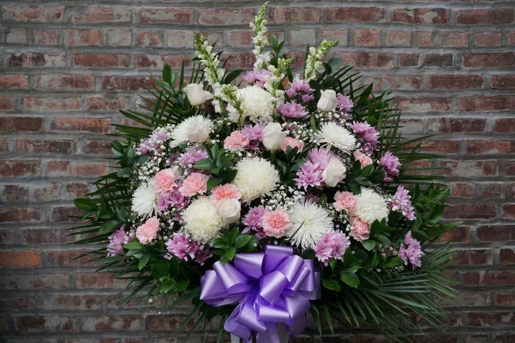 Large funeral spray of pink and white flowers with a purple bow