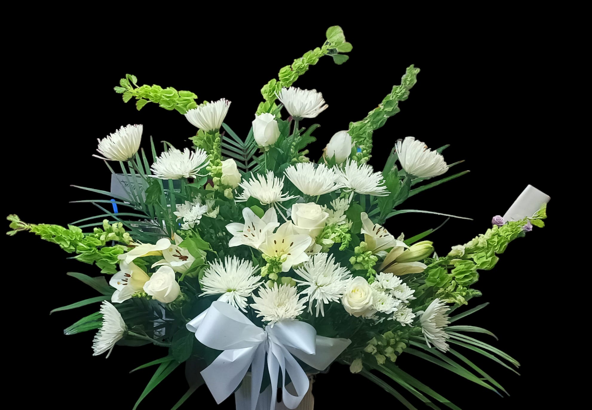 White floral arrangement with lilies, roses, and a white ribbon