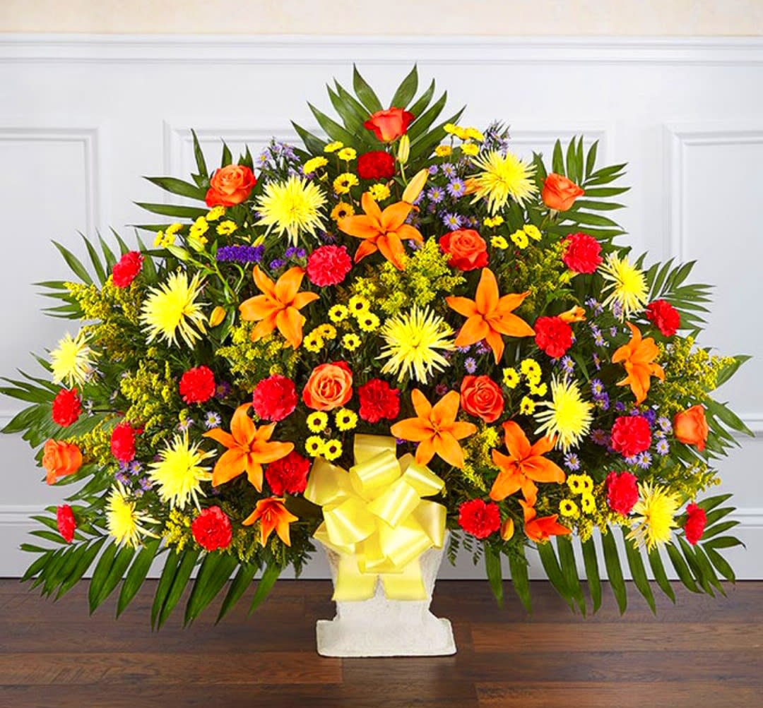 Large colorful floral spray with orange lilies and roses in a white pedestal vase