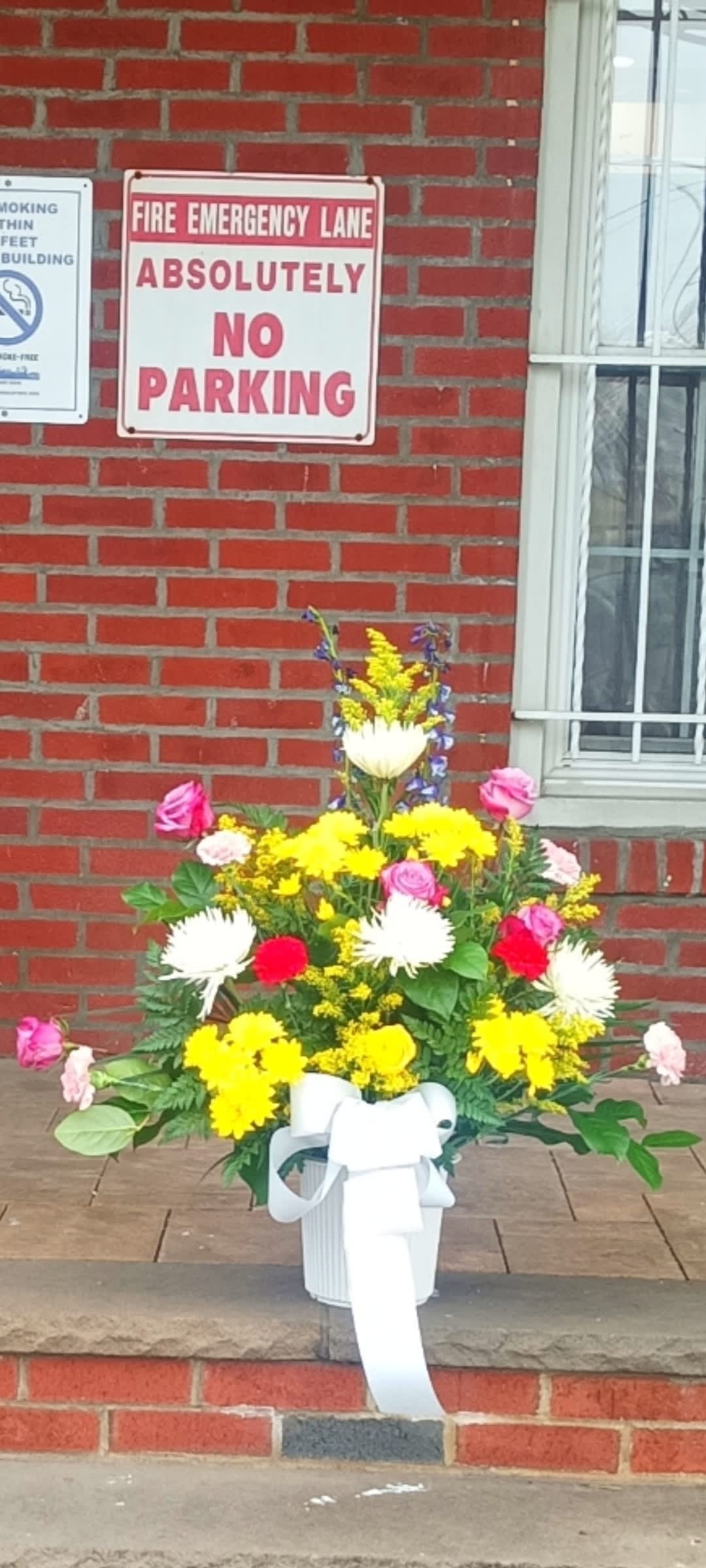Colorful mixed flower arrangement in a white container with a ribbon