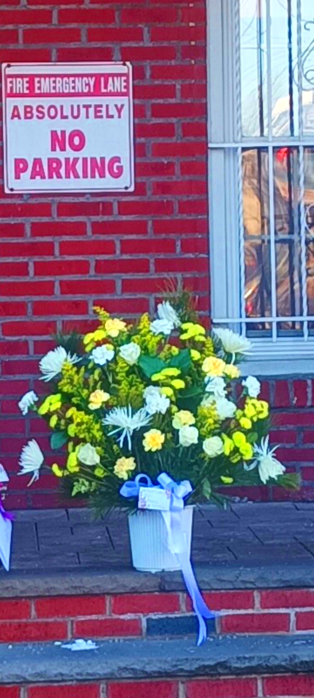 Yellow and white floral arrangement in a white vase with a blue ribbon