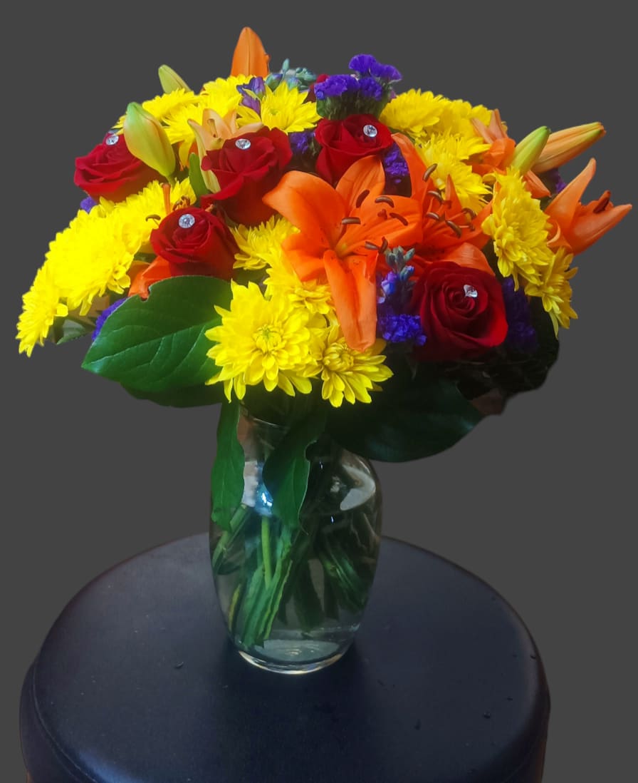 Bouquet of red roses, orange lilies, and yellow mums in a glass vase