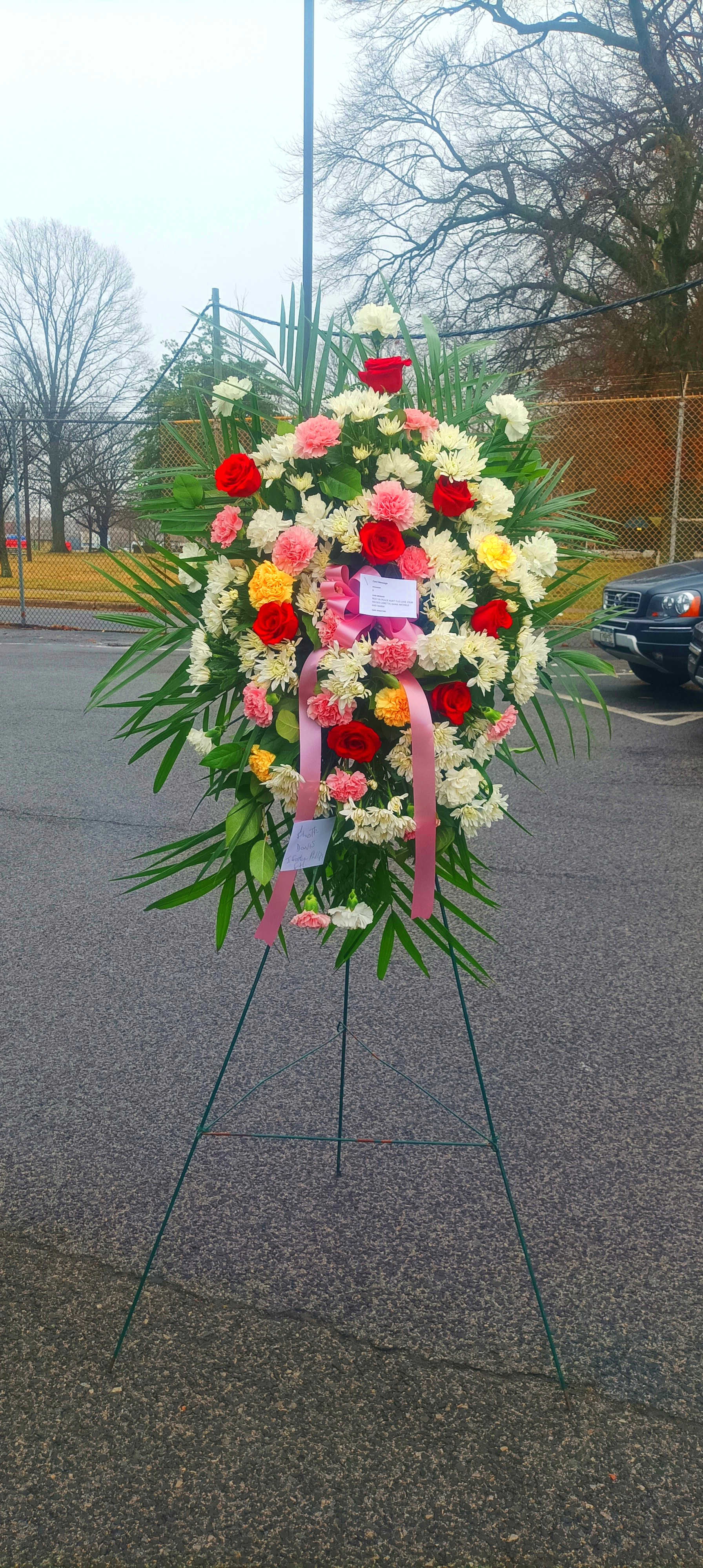 Large standing floral wreath with red, pink, and white flowers on an easel