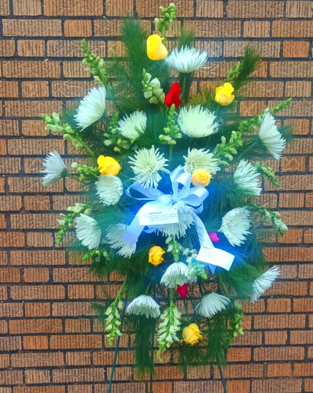 Standing floral spray with white blooms, yellow roses, and blue ribbon