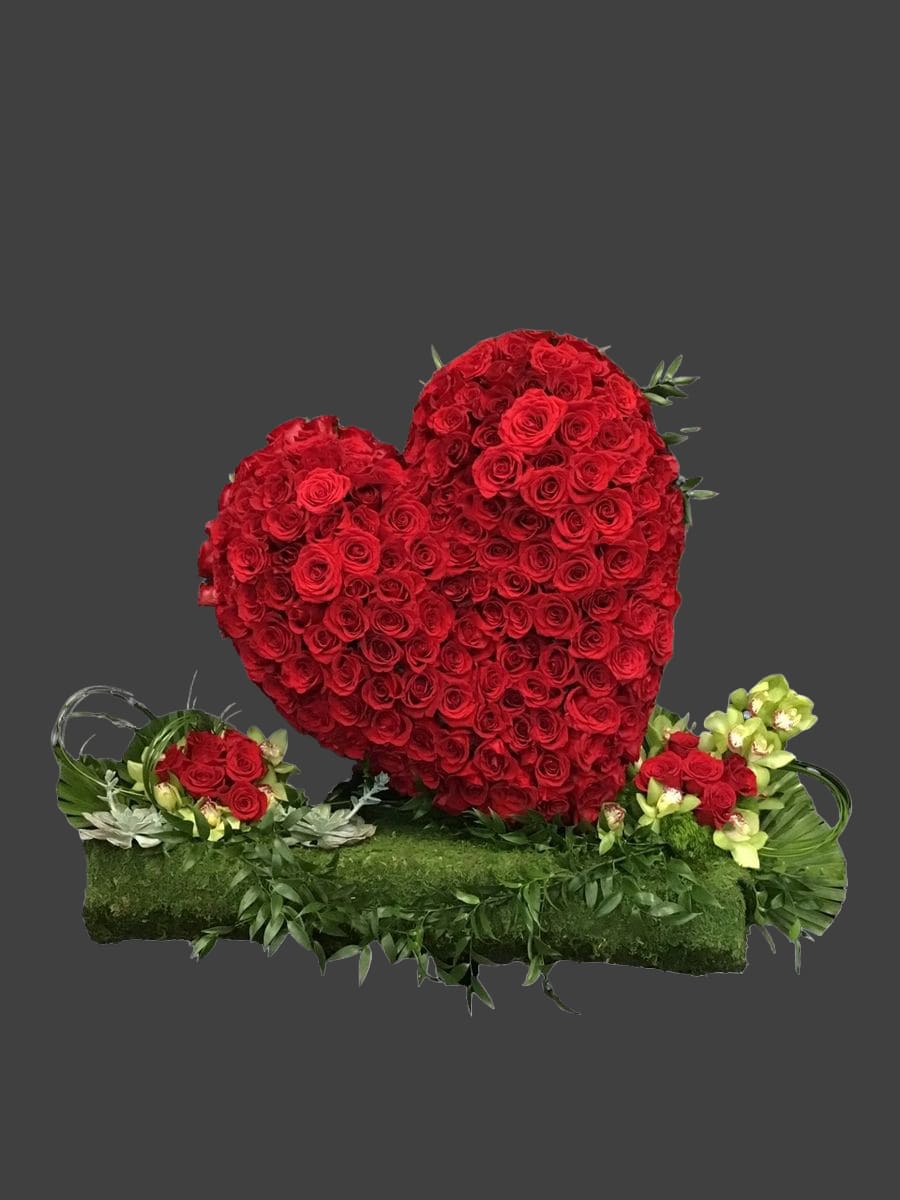 Heart-shaped red rose arrangement on a green base with small side bouquets