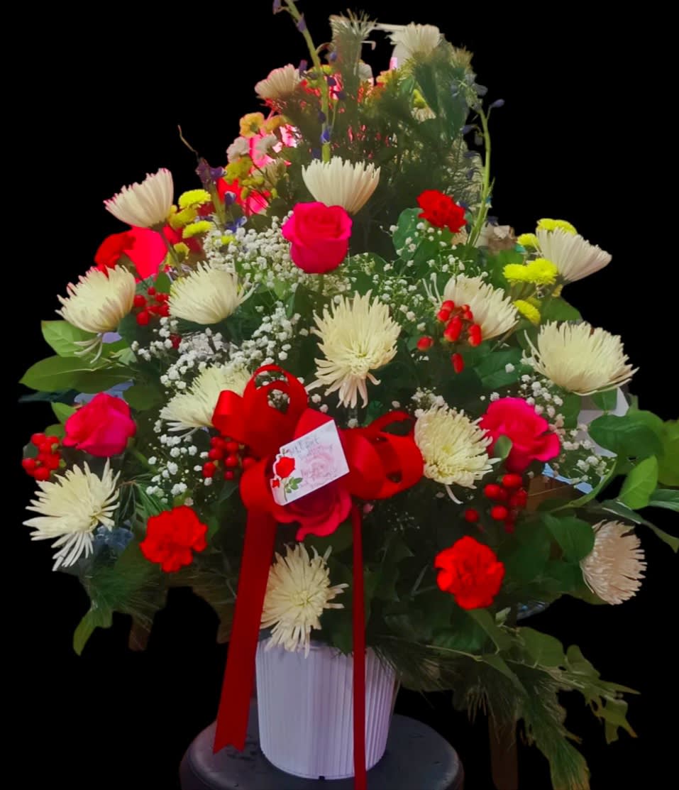 Large mixed flower arrangement in a white vase with a red ribbon