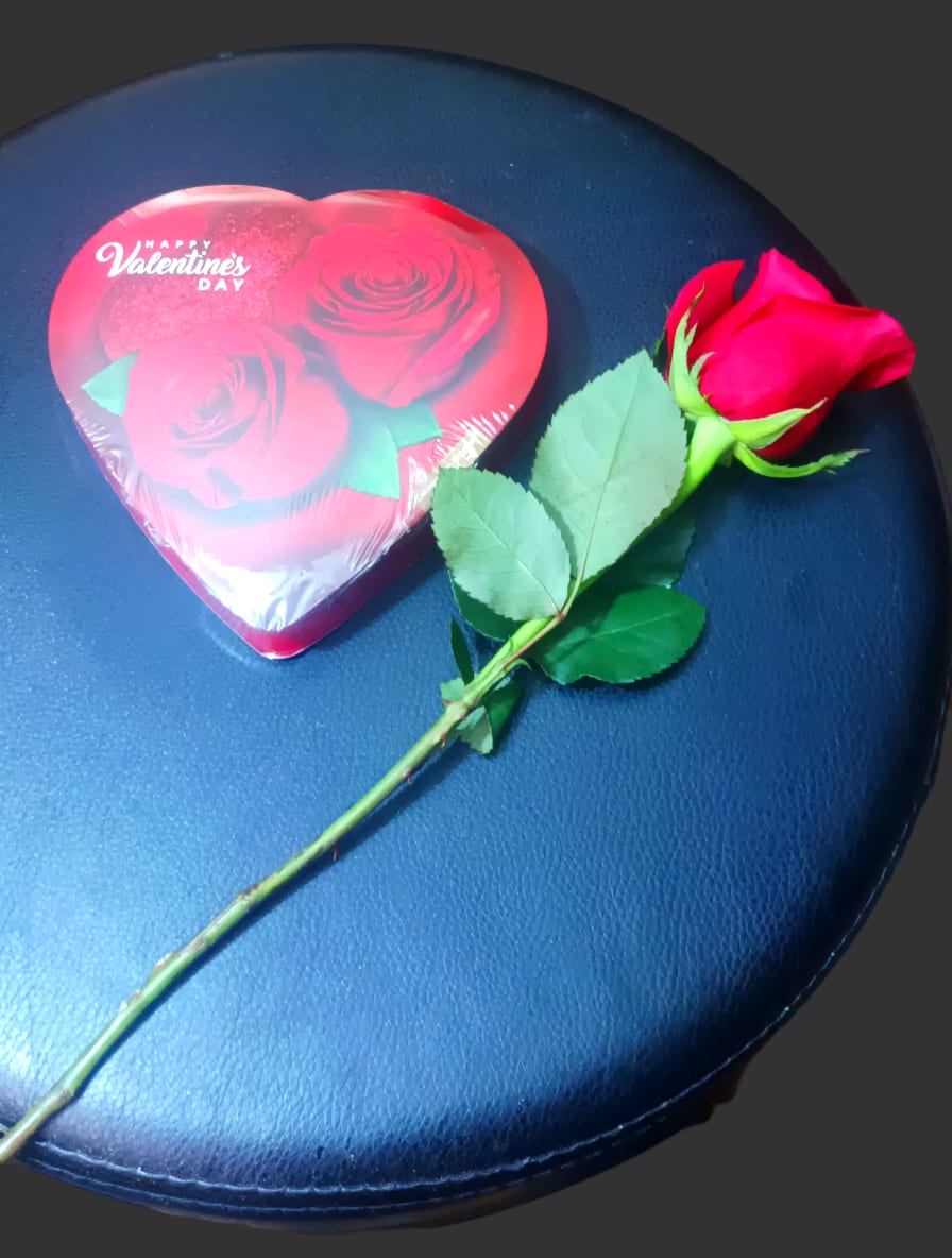 Single red rose beside a heart-shaped Valentine candy box
