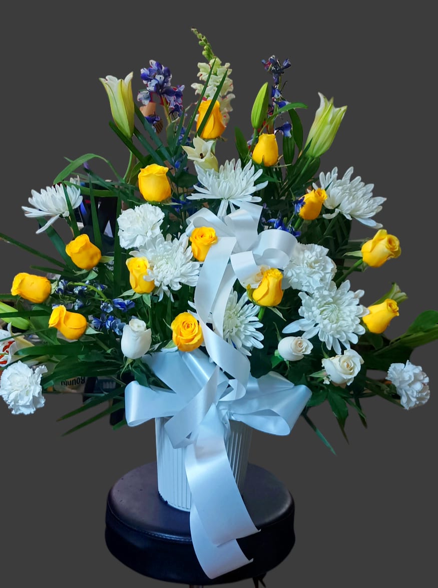 Bouquet of yellow and white flowers in a white vase with a blue ribbon