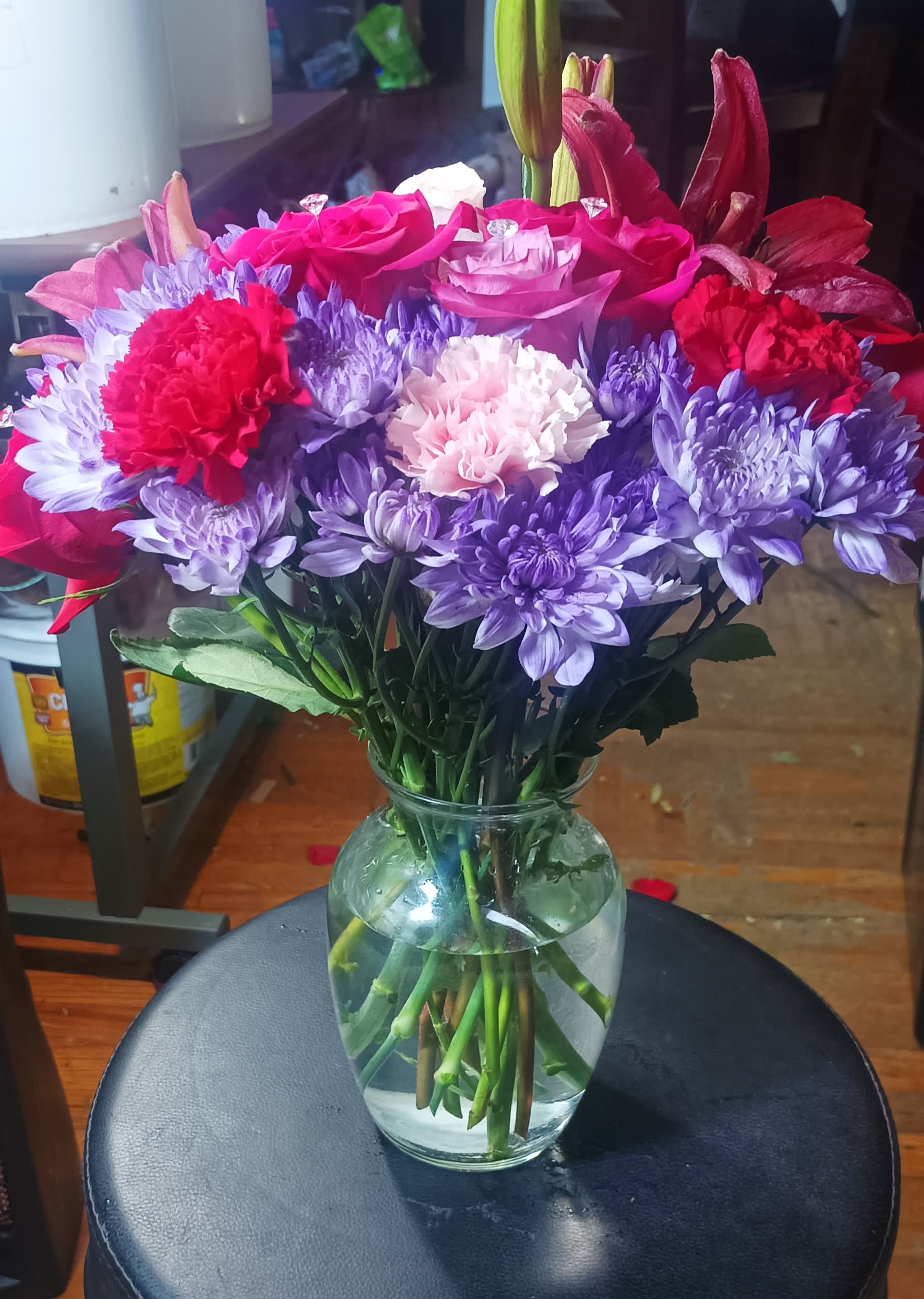 Mixed bouquet of pink roses, purple chrysanthemums, and red carnations in a glass vase