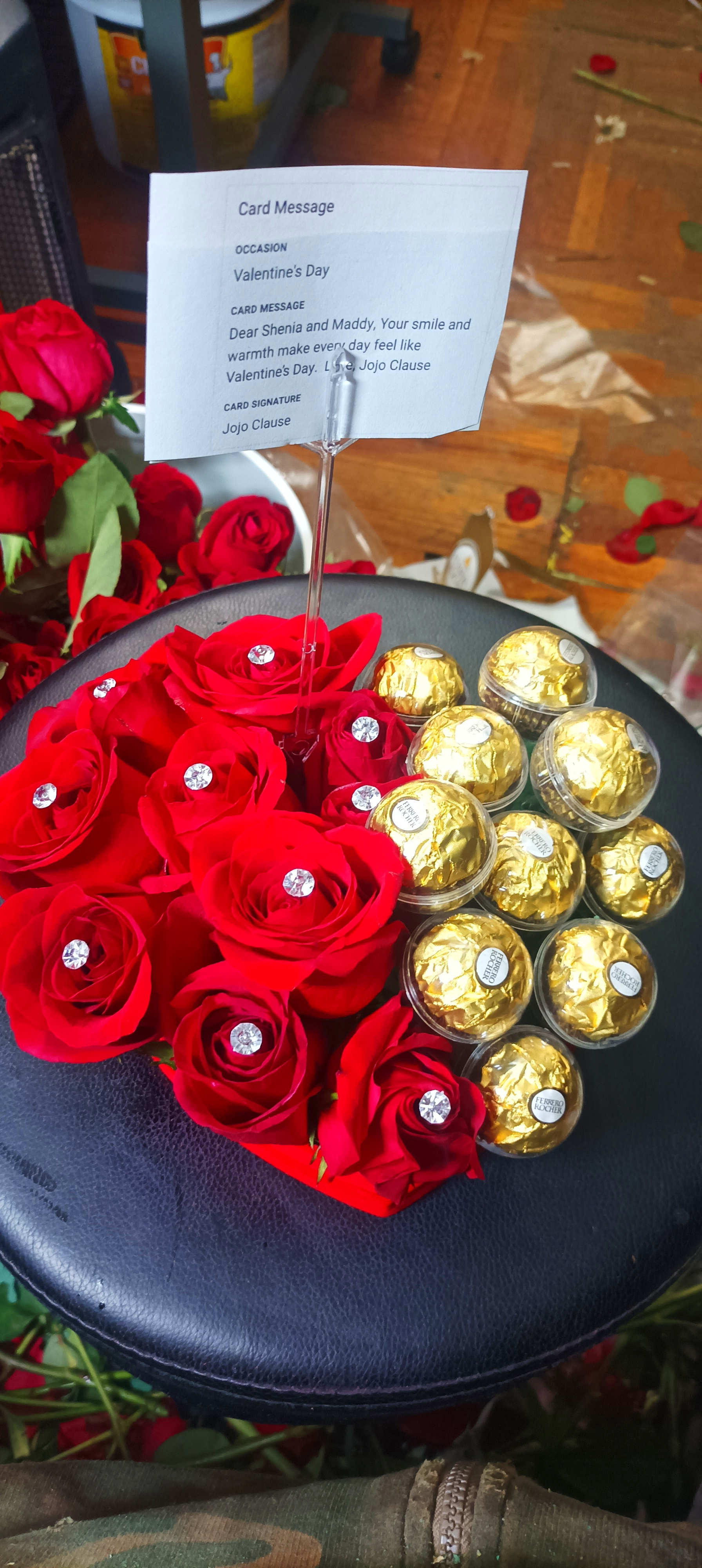 Red roses and gold-wrapped chocolates arranged on a black round box with a card.
