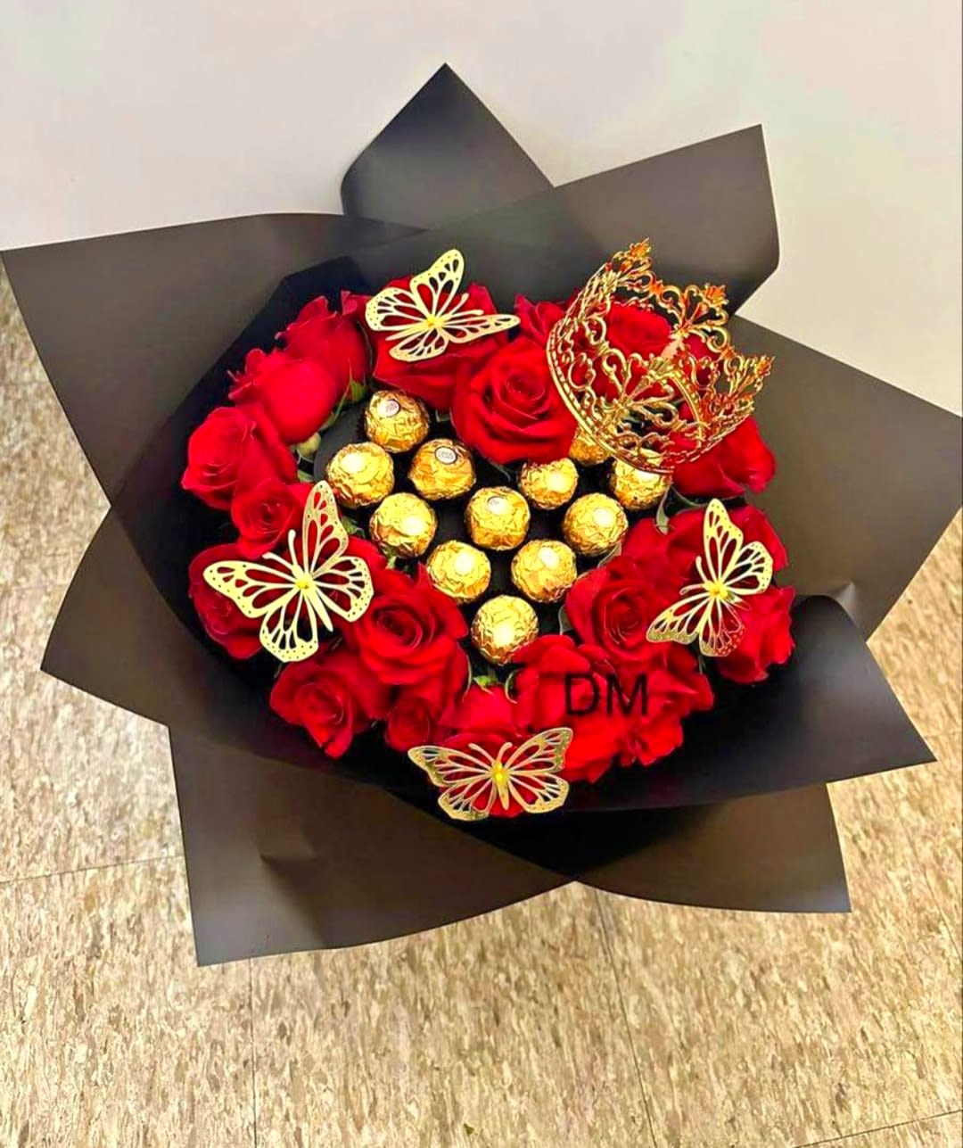 Red roses arranged with gold-wrapped chocolates in black paper
