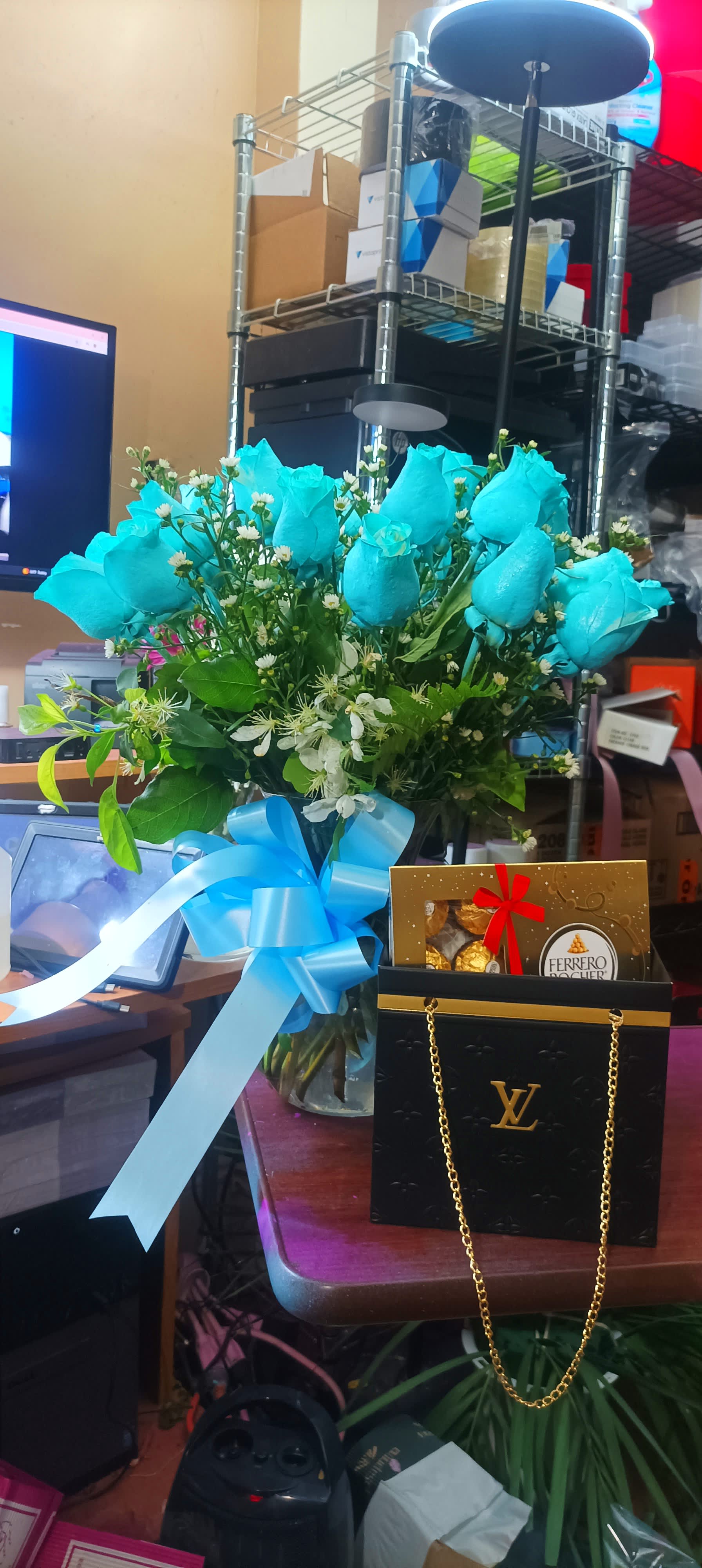 Blue roses in a glass vase with a ribbon and chocolates in a gift bag