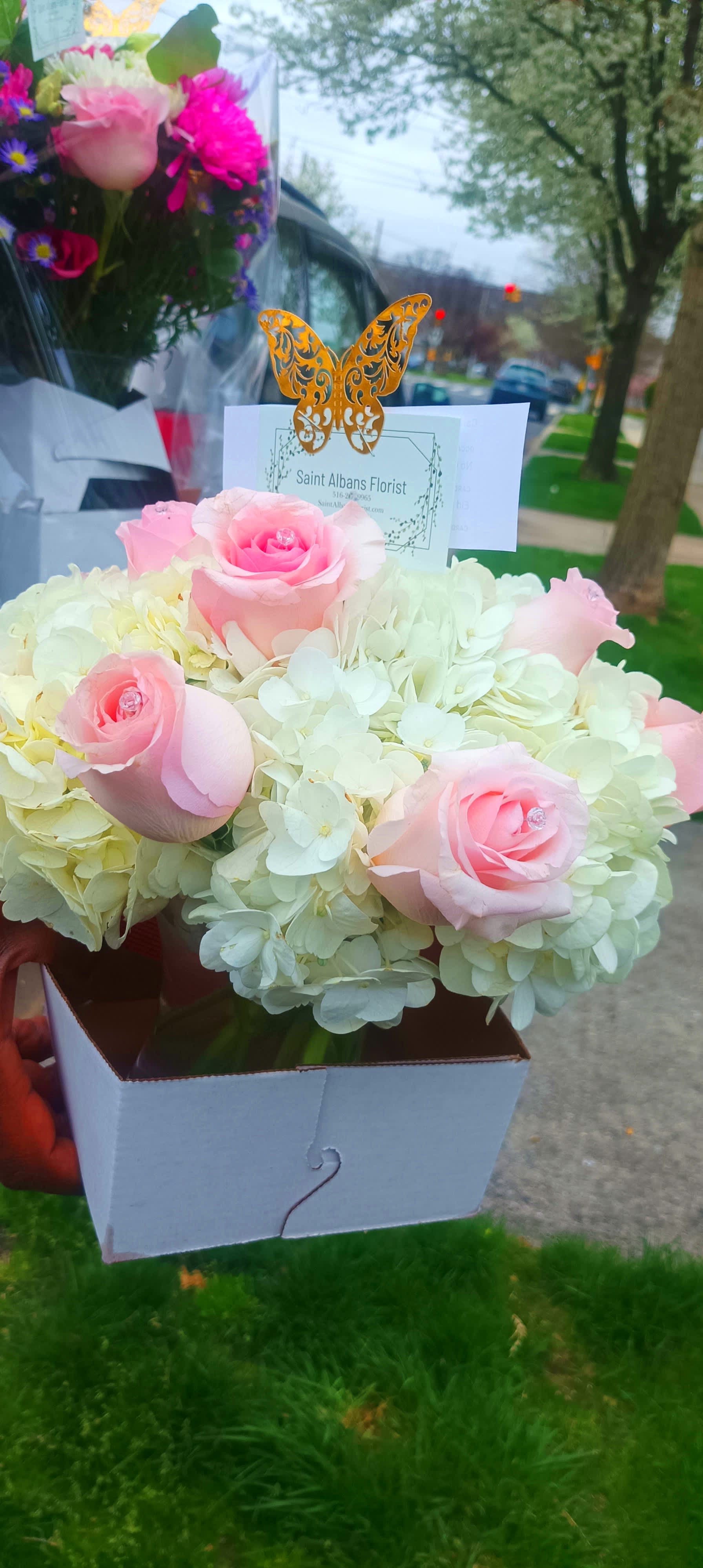 Pink roses in a white box with pale hydrangeas and a butterfly card topper