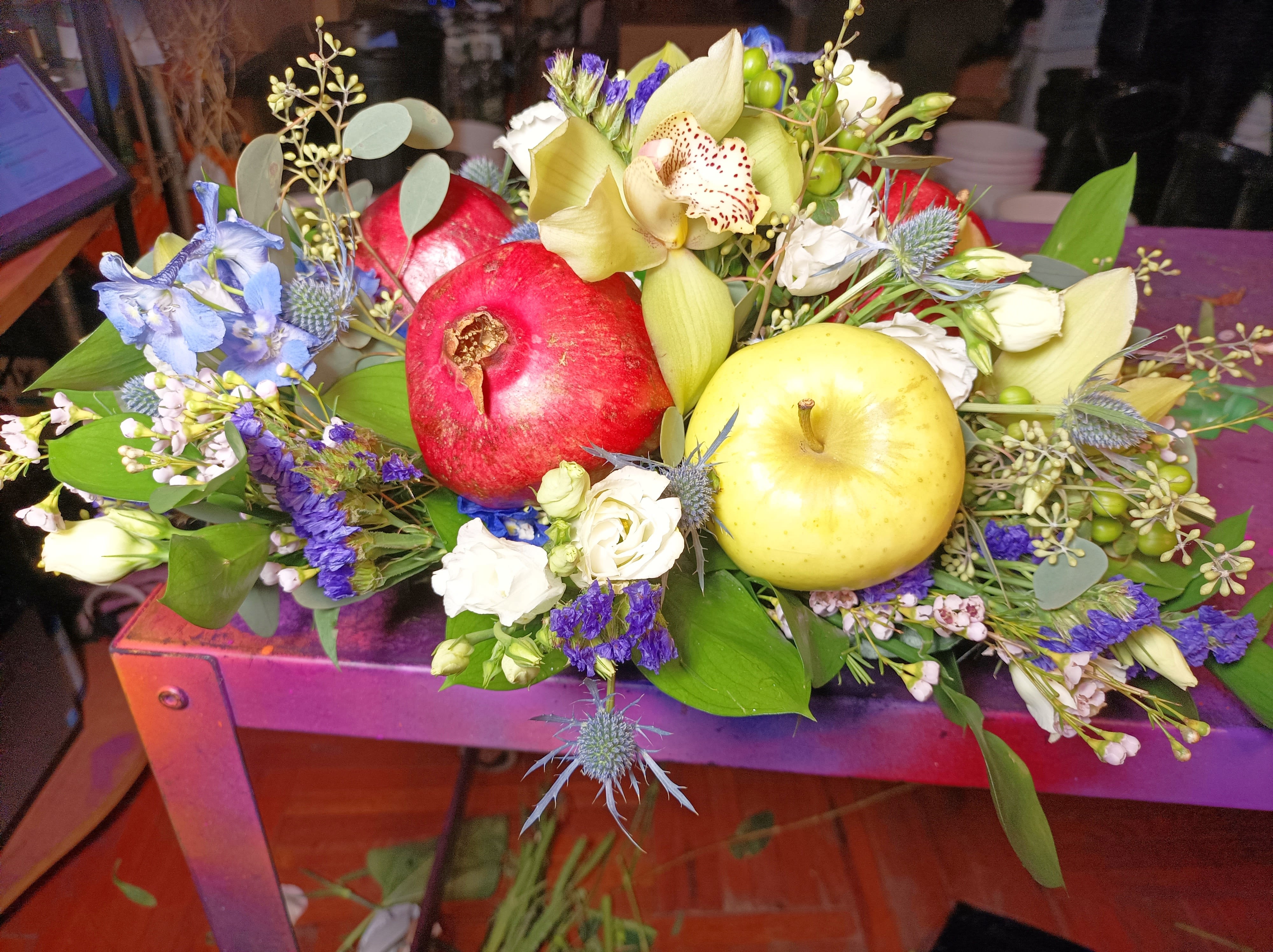 Mixed floral arrangement with pomegranates and apples on a purple table