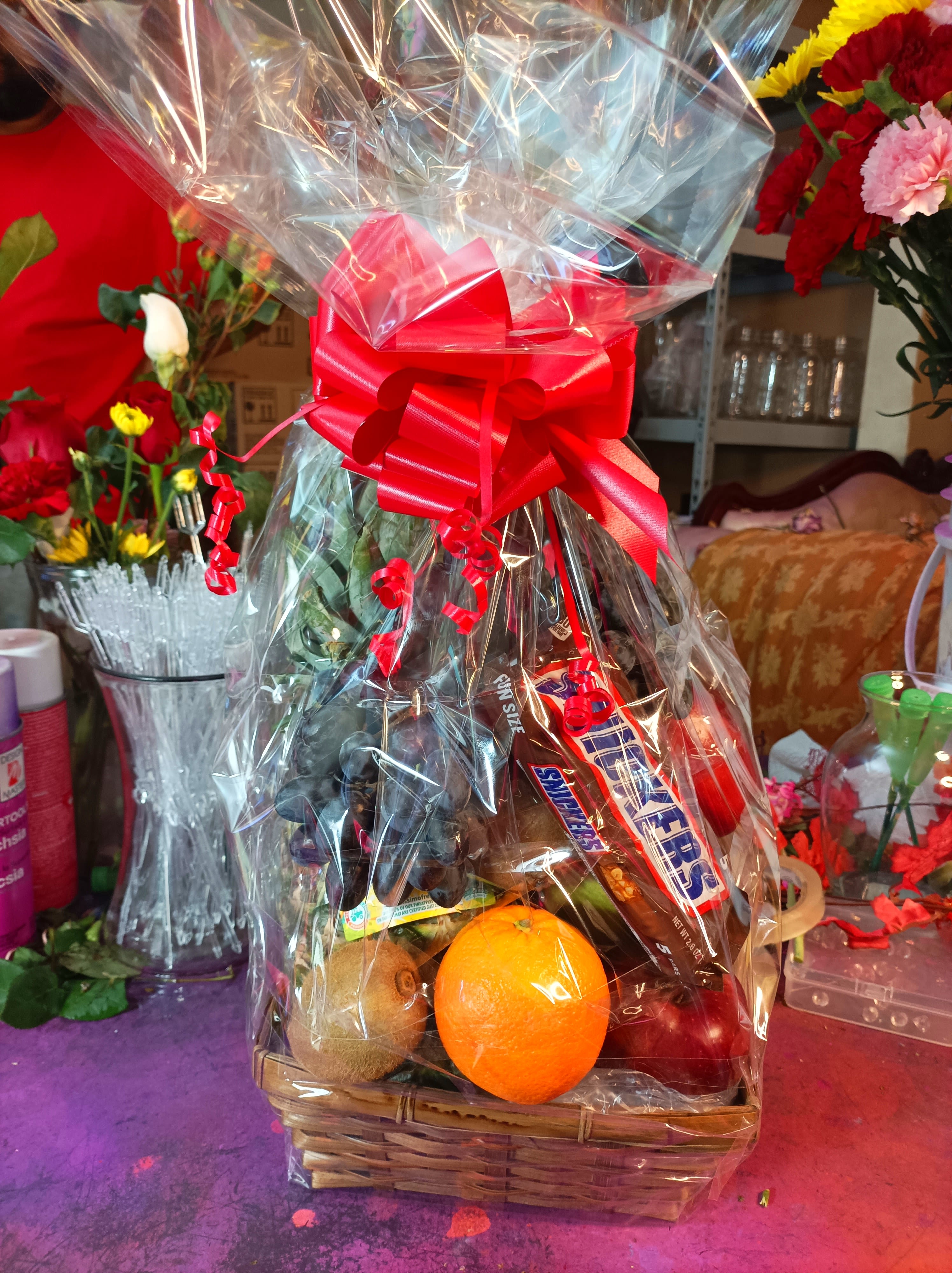 Gift basket with fruit and candy wrapped in clear cellophane and a red bow