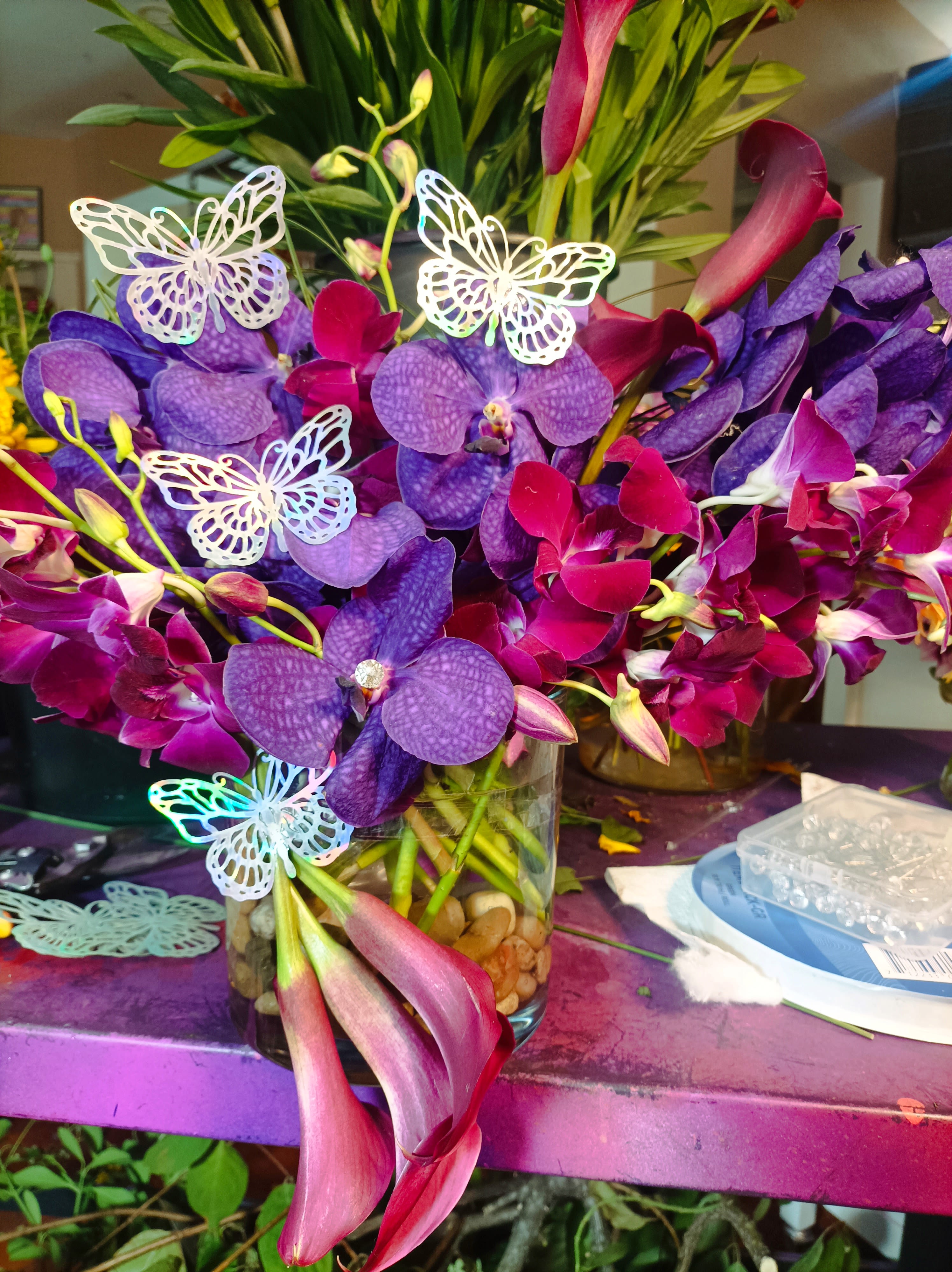 Purple orchids and pink calla lilies in a glass vase with butterfly picks