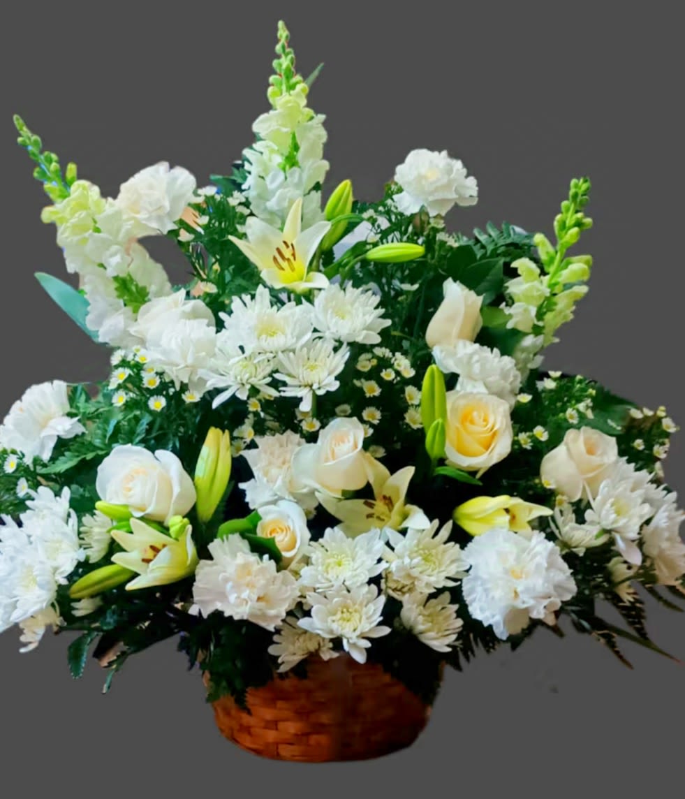 White floral arrangement in a woven basket with lilies and roses