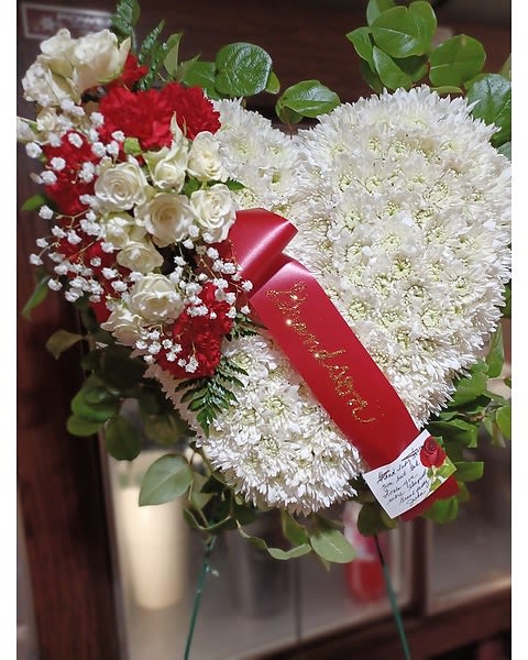 Heart-shaped white and red floral arrangement with a red ribbon