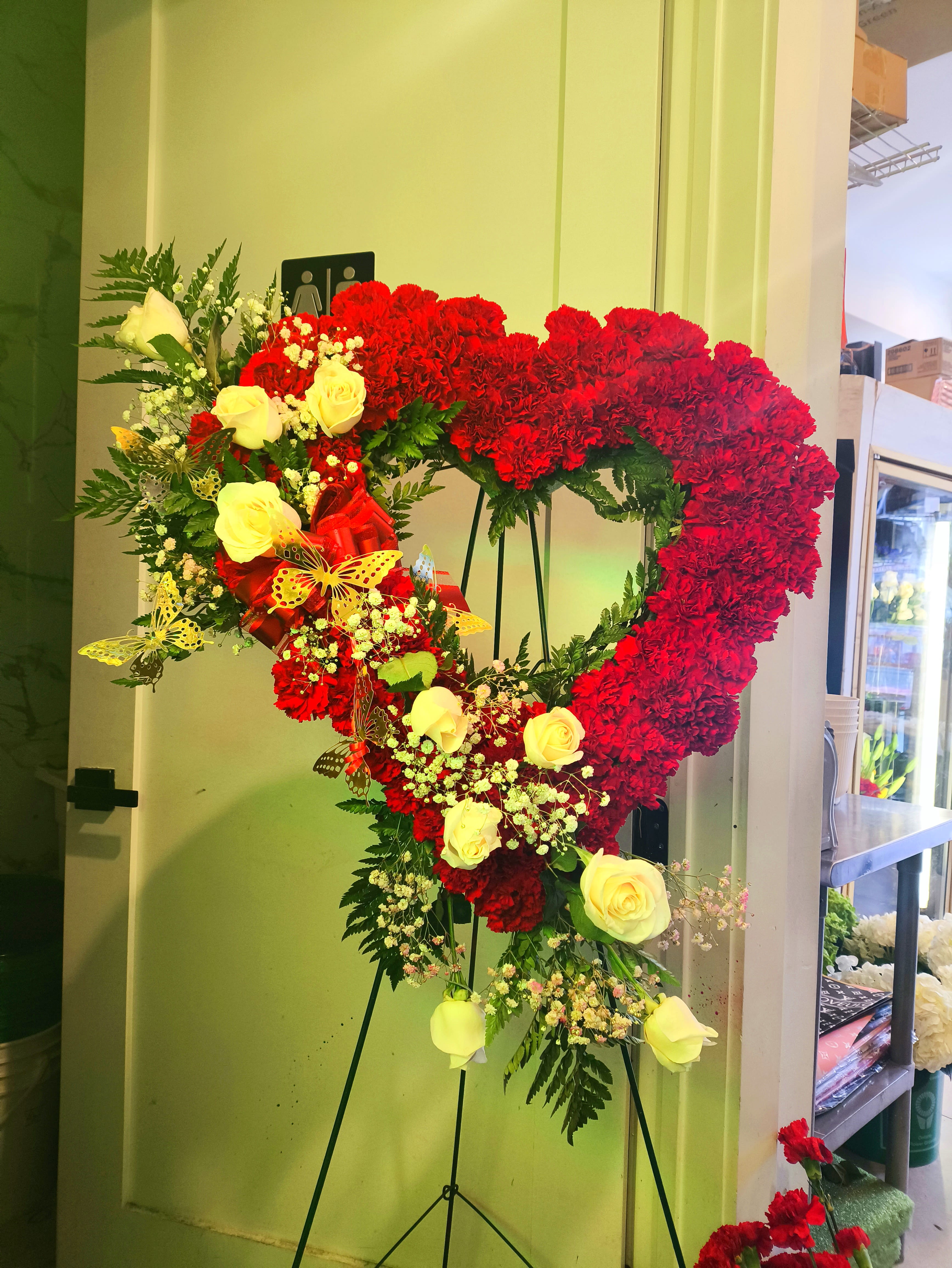 Heart-shaped floral standing arrangement with red carnations and yellow roses