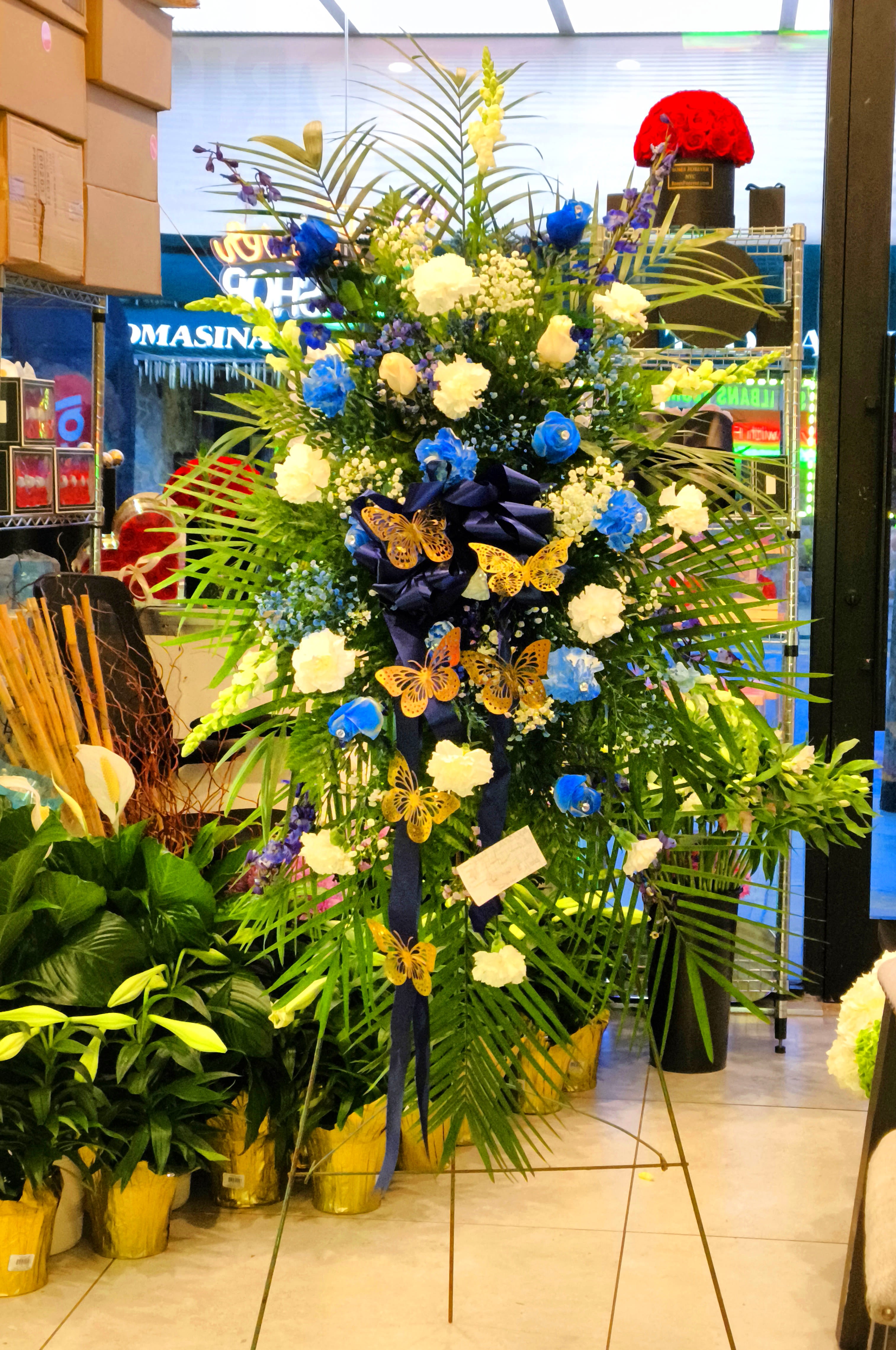 Tall floral standing spray with blue and white flowers and butterfly accents