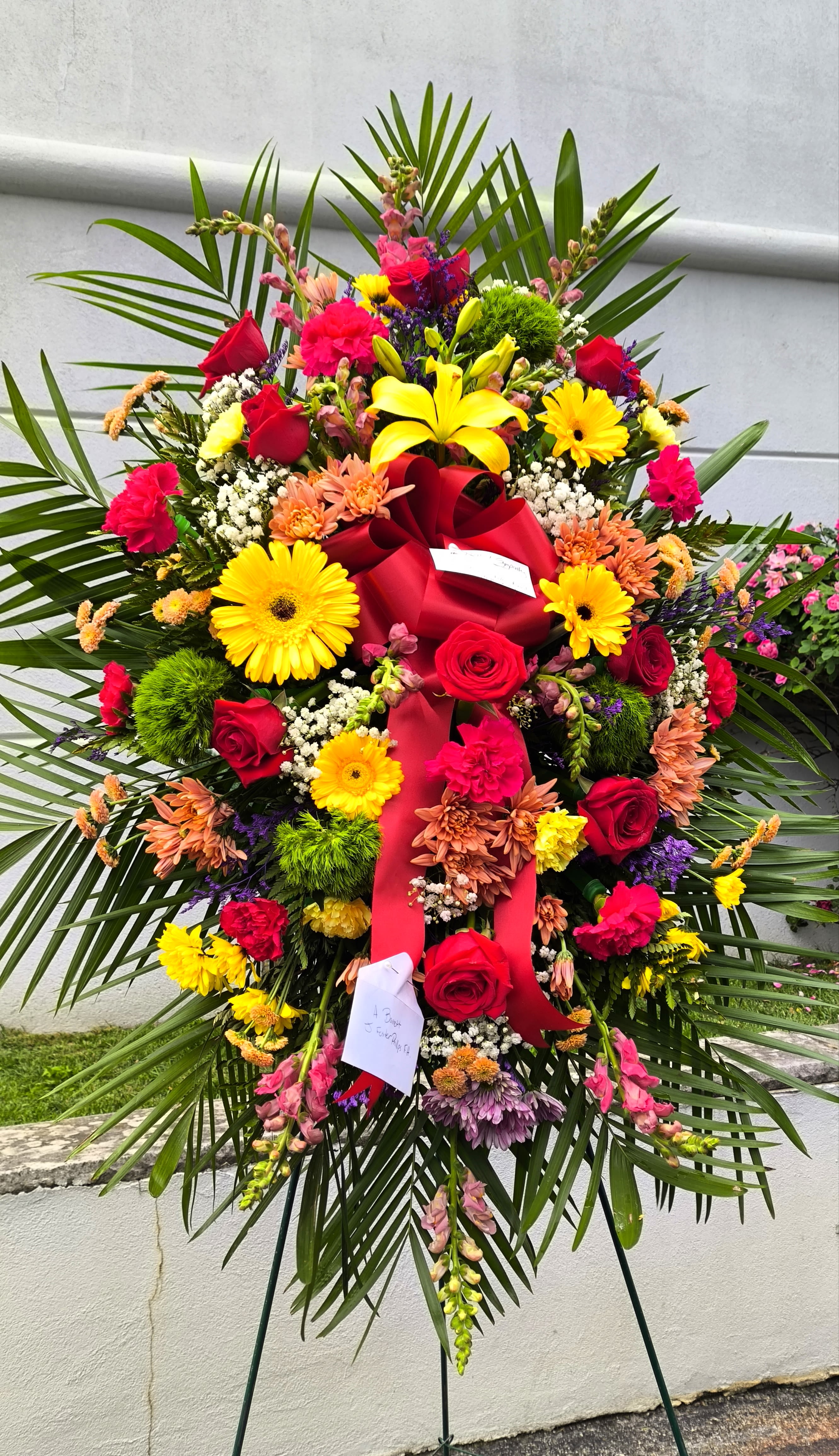 Large standing floral spray with red roses and yellow lilies on a red ribboned easel