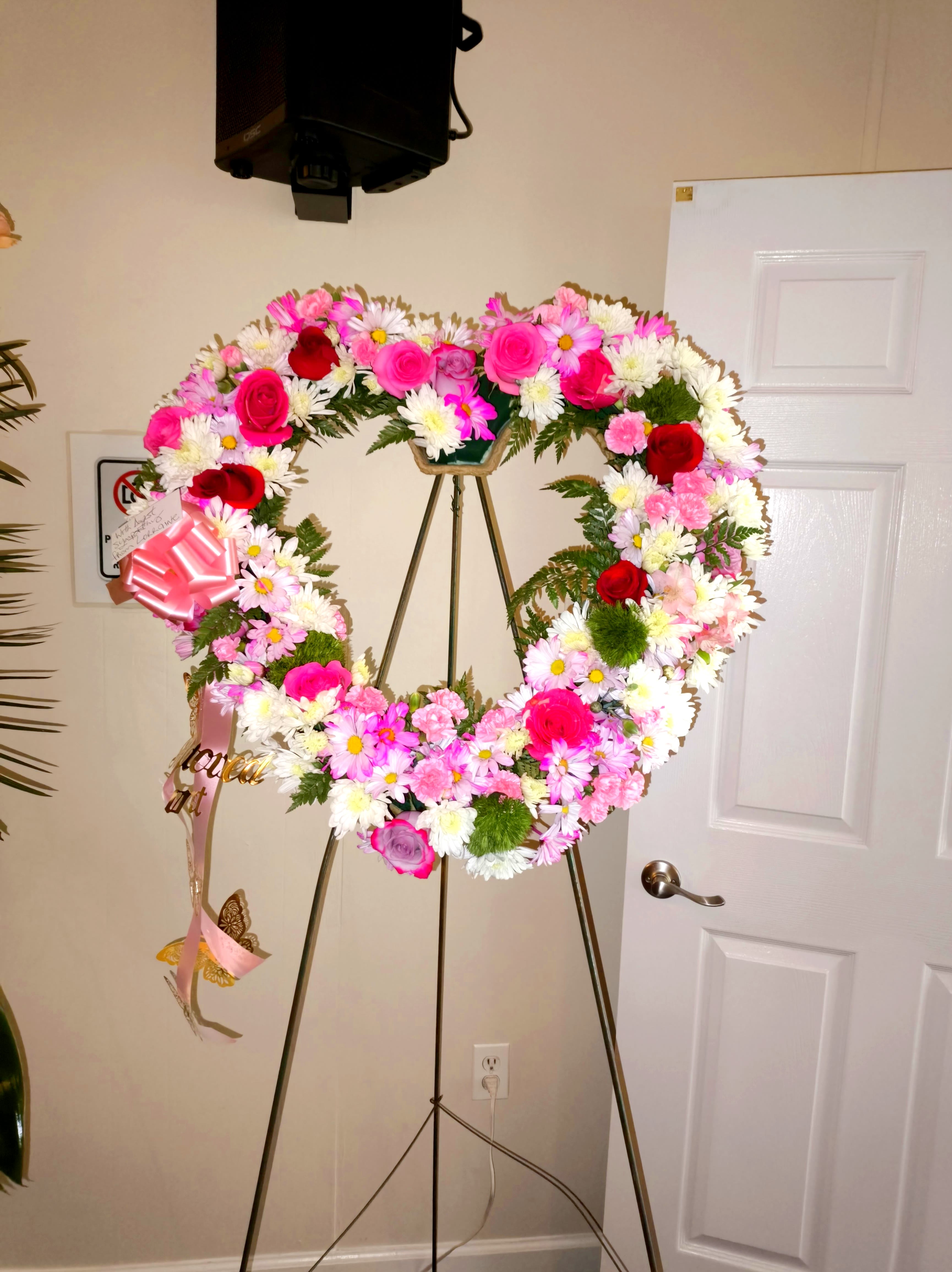 Heart-shaped floral wreath on a stand with pink, white, and red flowers