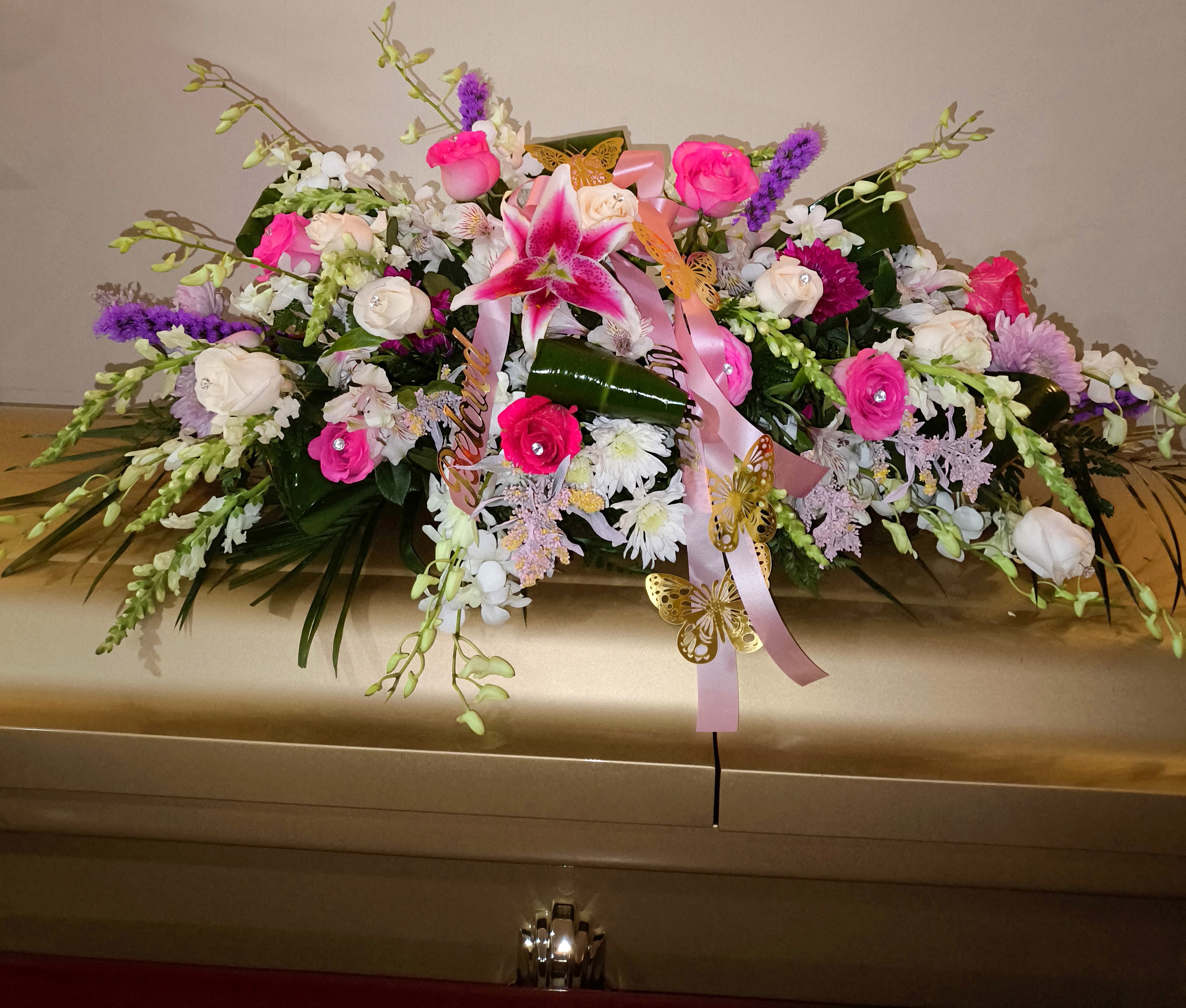 Pink and white floral casket spray with ribbons and butterfly accents