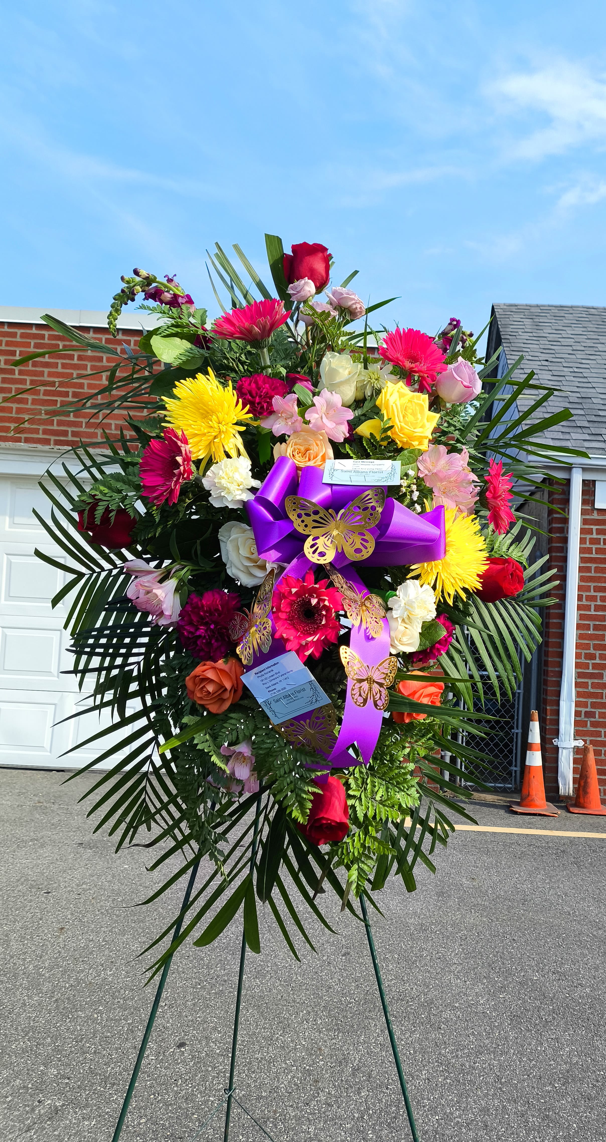 Large standing floral spray with bright mixed flowers and purple ribbon