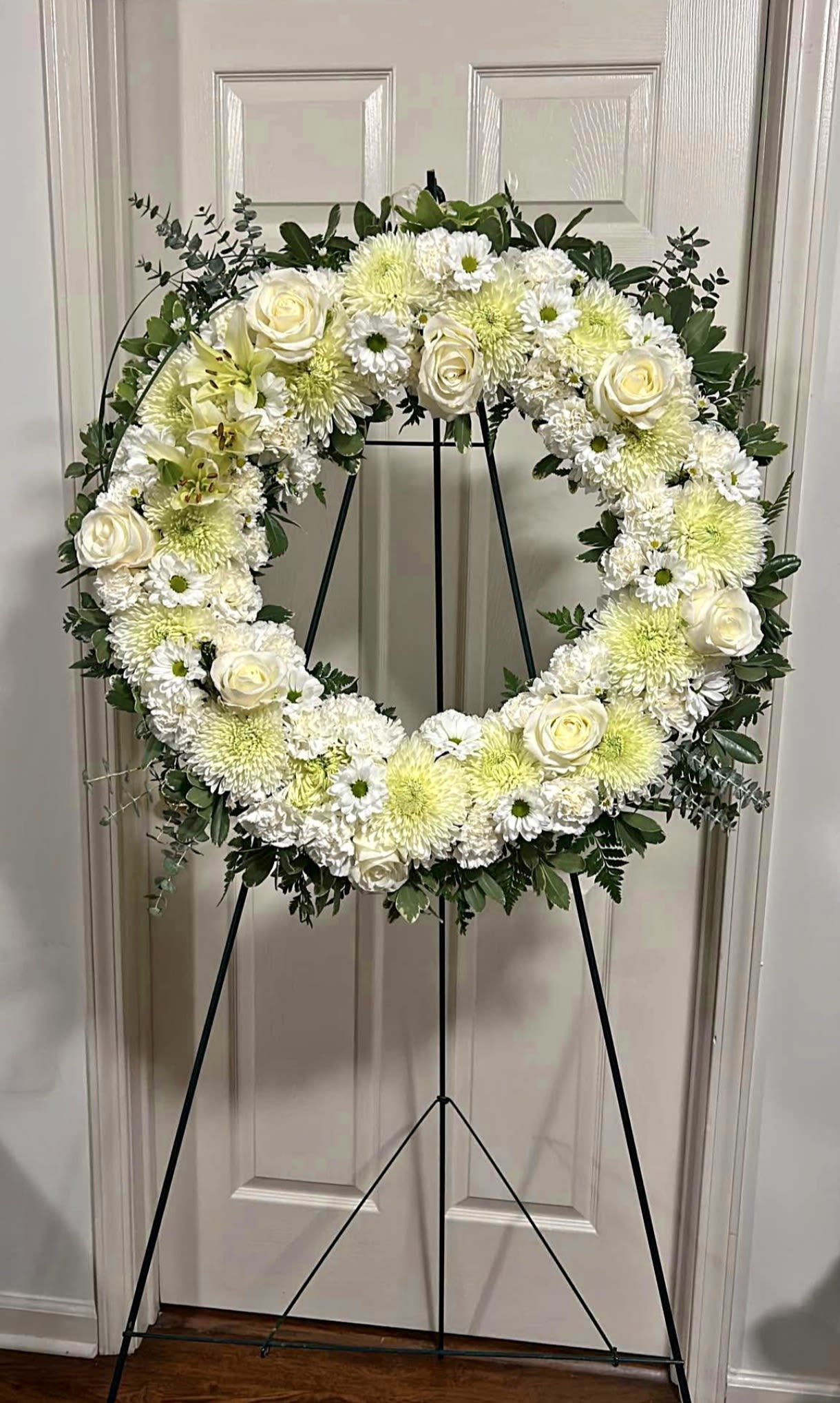 White floral wreath on a black stand with roses and mums