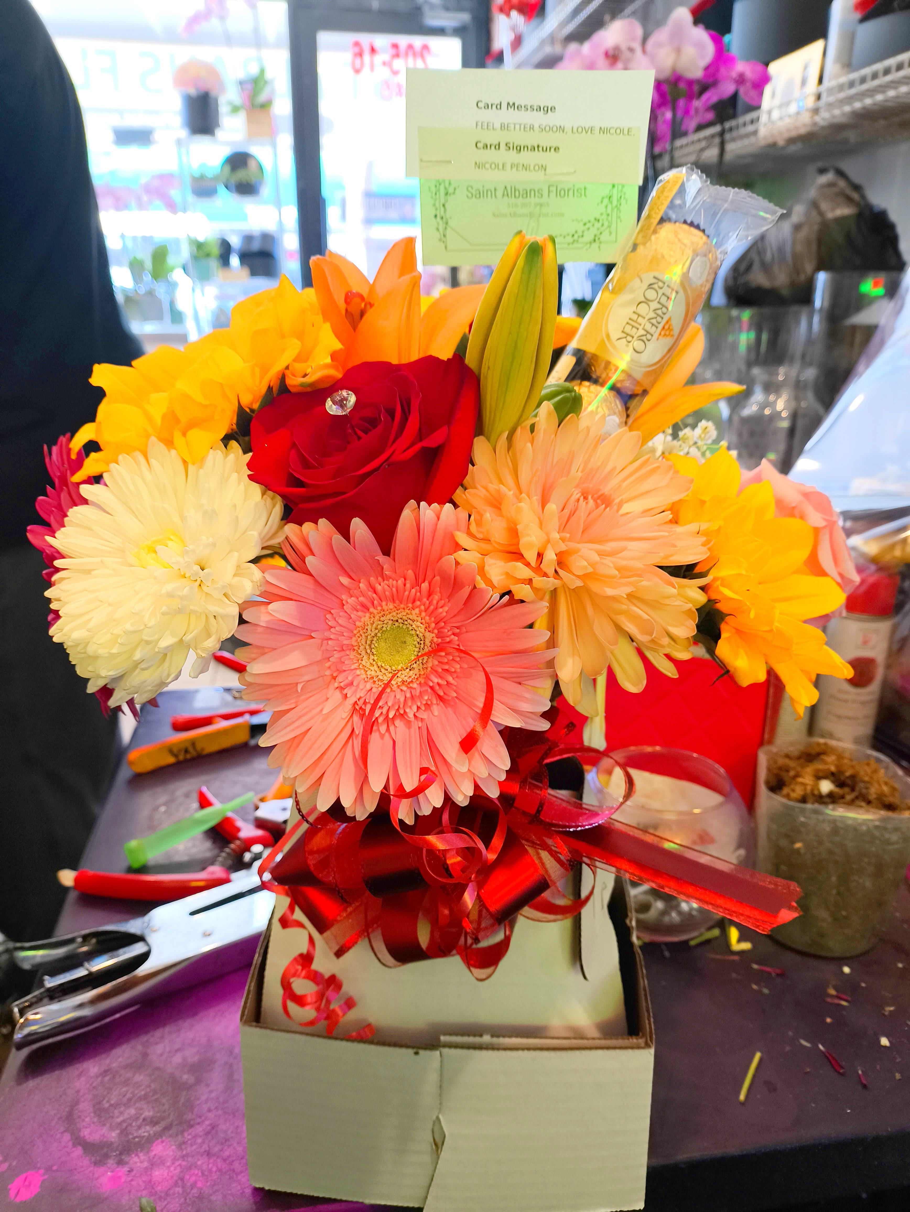 Bright mixed bouquet with a red rose, gerbera daisy, lilies, and chrysanthemums in a gift box.