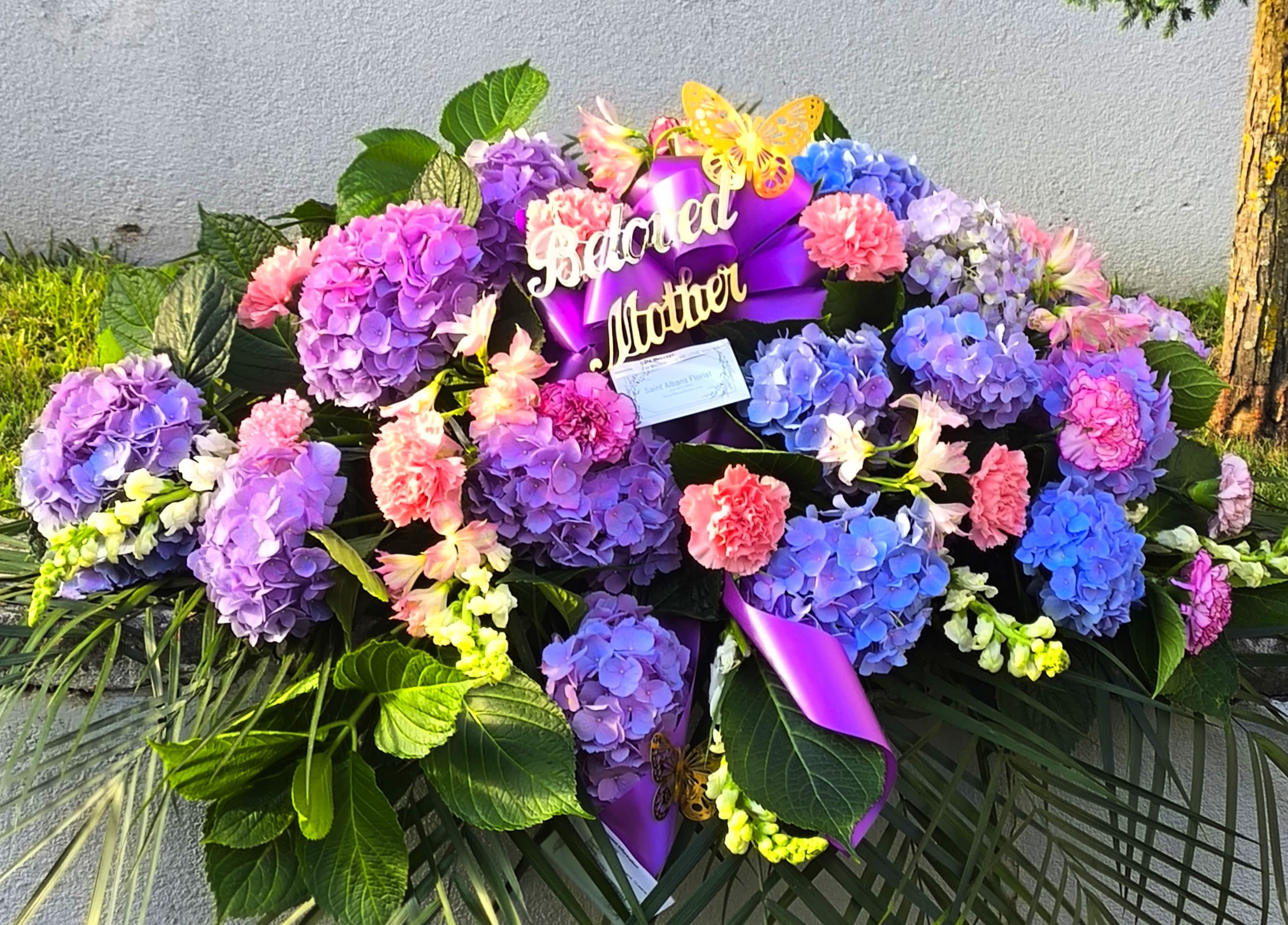 Large floral arrangement with purple hydrangeas, pink carnations, and a purple ribbon