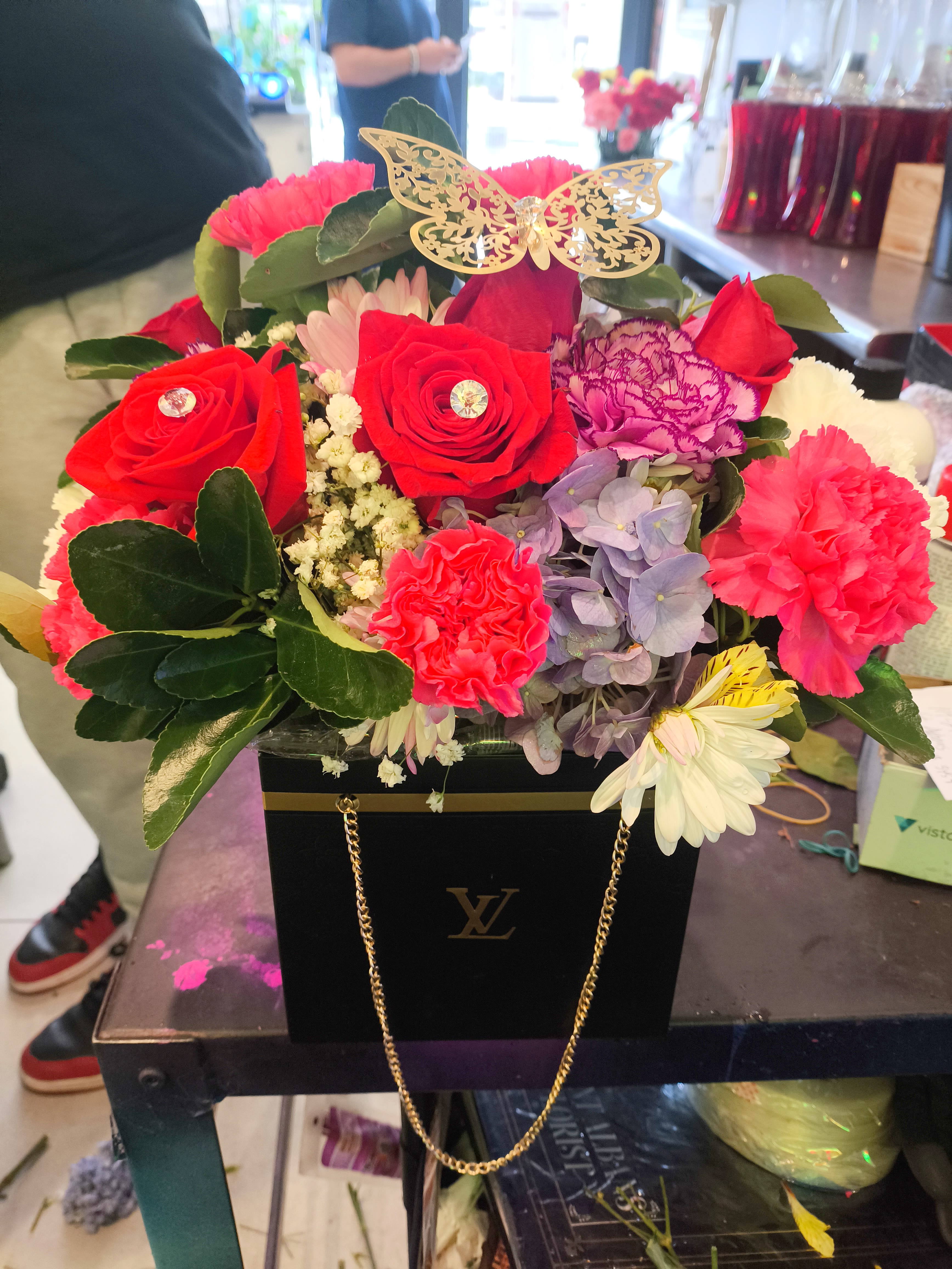 Bright mixed flower arrangement in a black gift box with a gold butterfly topper