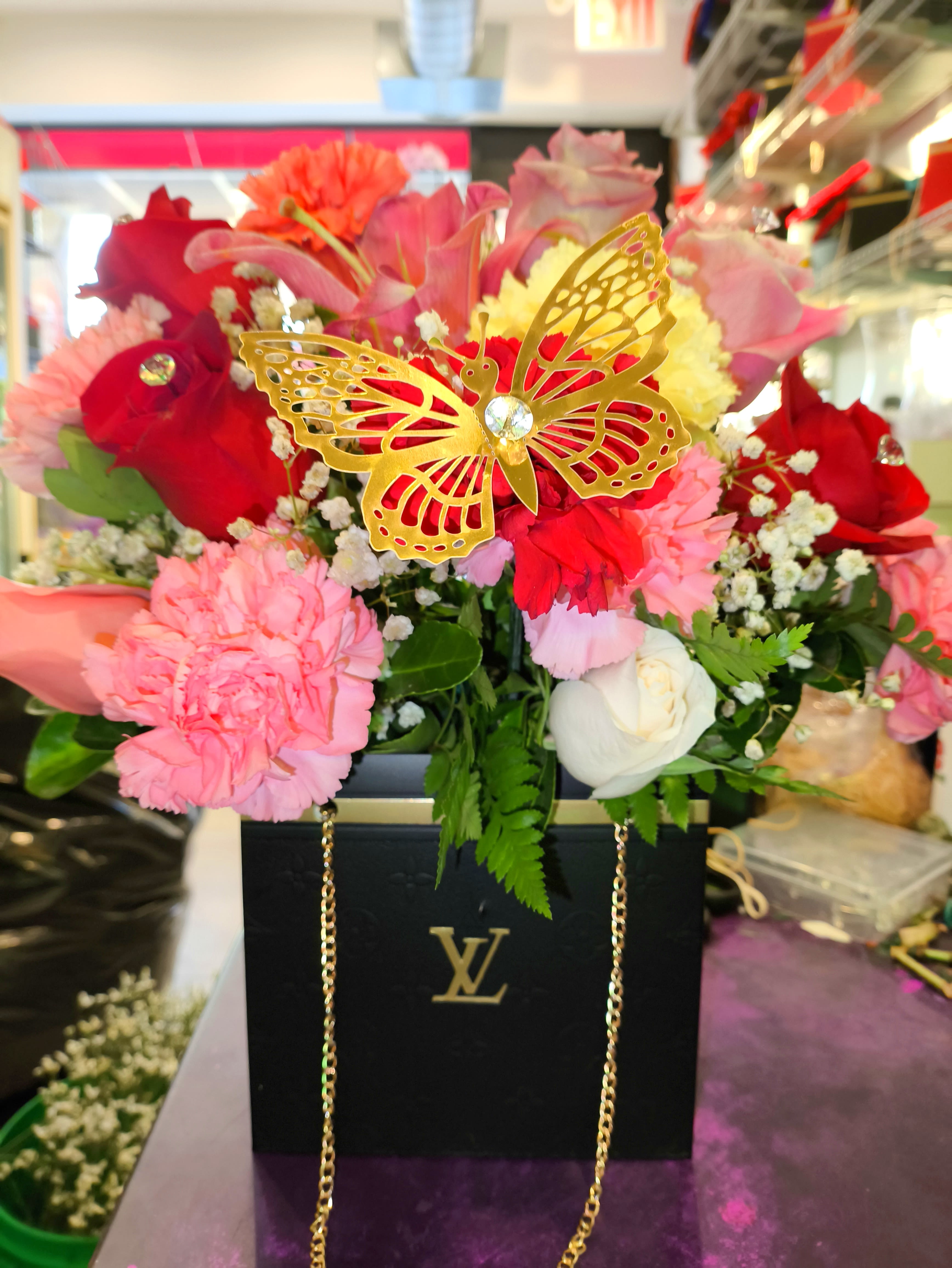 Mixed pink and red flower arrangement in a black box with a gold butterfly
