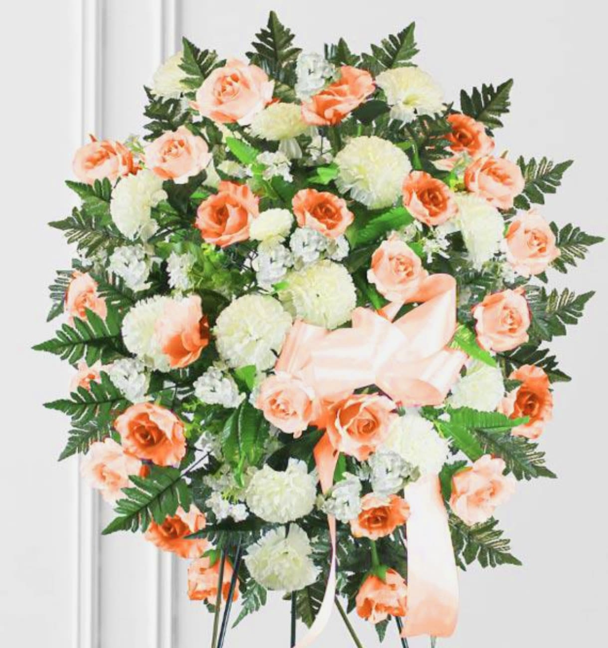 Peach roses and white carnations arranged in a standing wreath with a ribbon