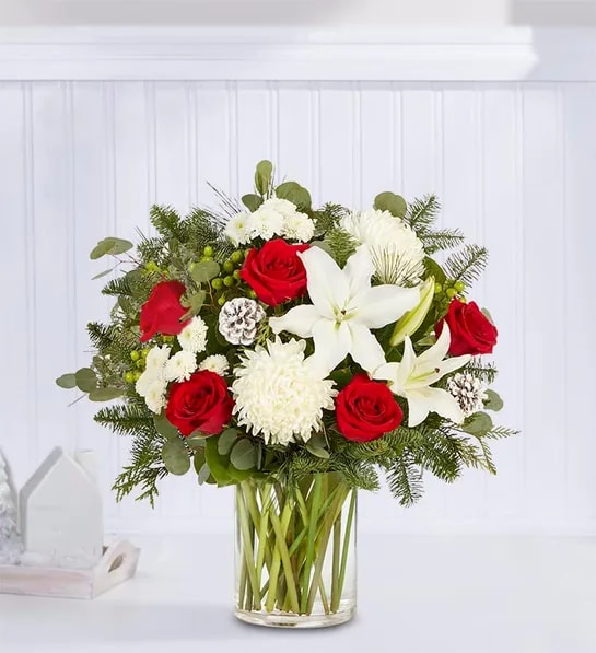Garden of Grandeur Holiday - The signature colors of Christmas are on display in our grand holiday arrangement. Loosely gathered with an abundance of red &amp; white blooms, lush greenery and glistening, snow-tipped pinecones, it’s the perfect gift for celebrating the season in luxurious style.