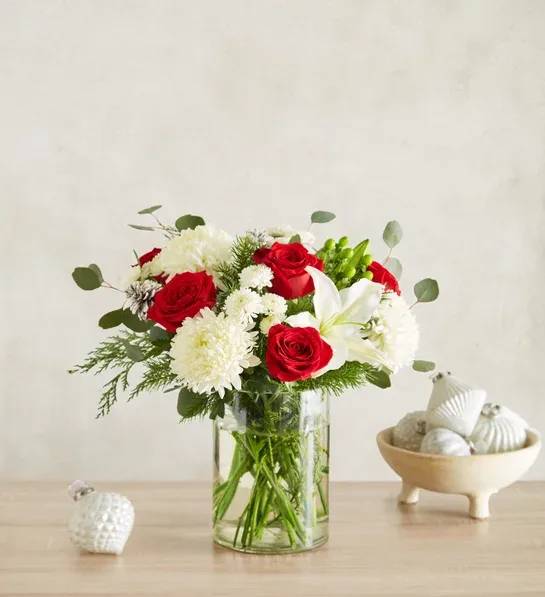 Garden of Grandeur for Holiday - The signature colors of Christmas are on display in our grand holiday arrangement. Loosely gathered with an abundance of red &amp; white blooms, lush greenery and glistening, snow-tipped pinecones, it’s the perfect gift for celebrating the season in luxurious style.