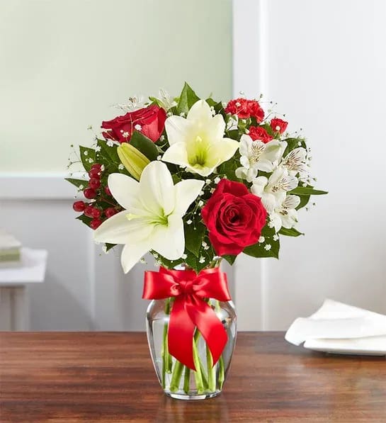 Arrangement of red roses and white lilies in a clear glass vase with a red ribbon bow