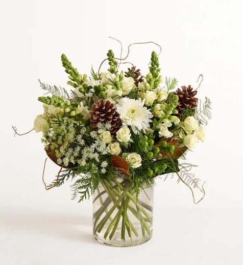 Aspen Joy - The beauty of the Rocky Mountains woodlands inspired this quietly luxurious arrangement. White spray roses, snapdragons, and other blooms are gathered among winter greenery and festive foliage in a sleek clear glass vase. It’s a gift as sophisticated as it is thoughtful.