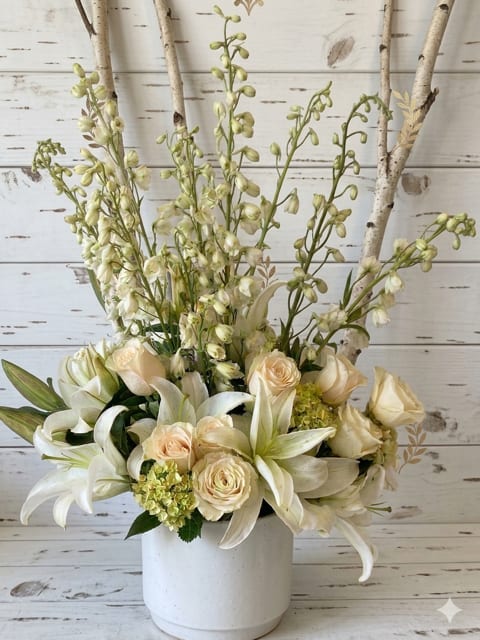 White lilies and cream roses in a white pot with tall birch branches.