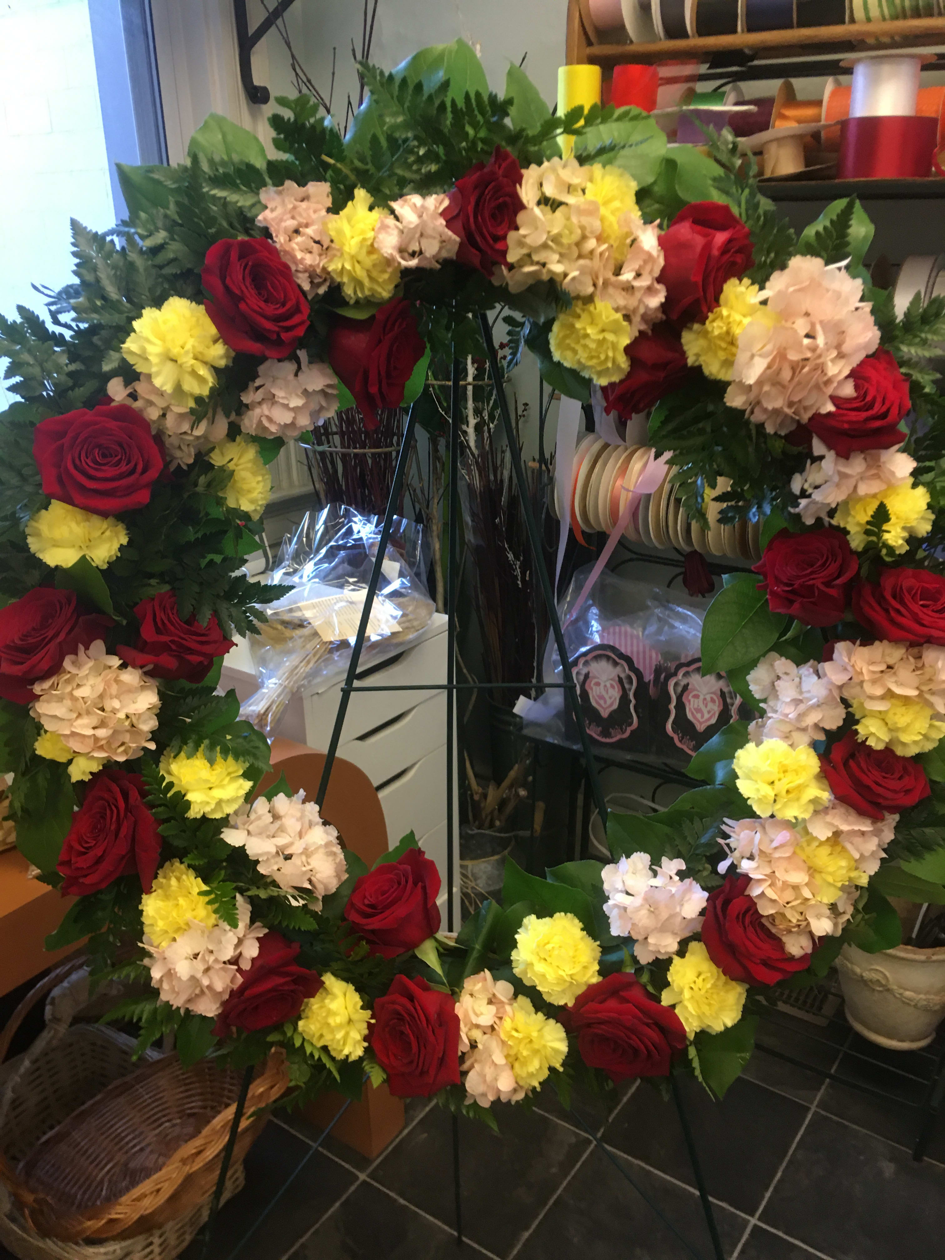 Large floral wreath with red roses, yellow carnations, and pale hydrangeas