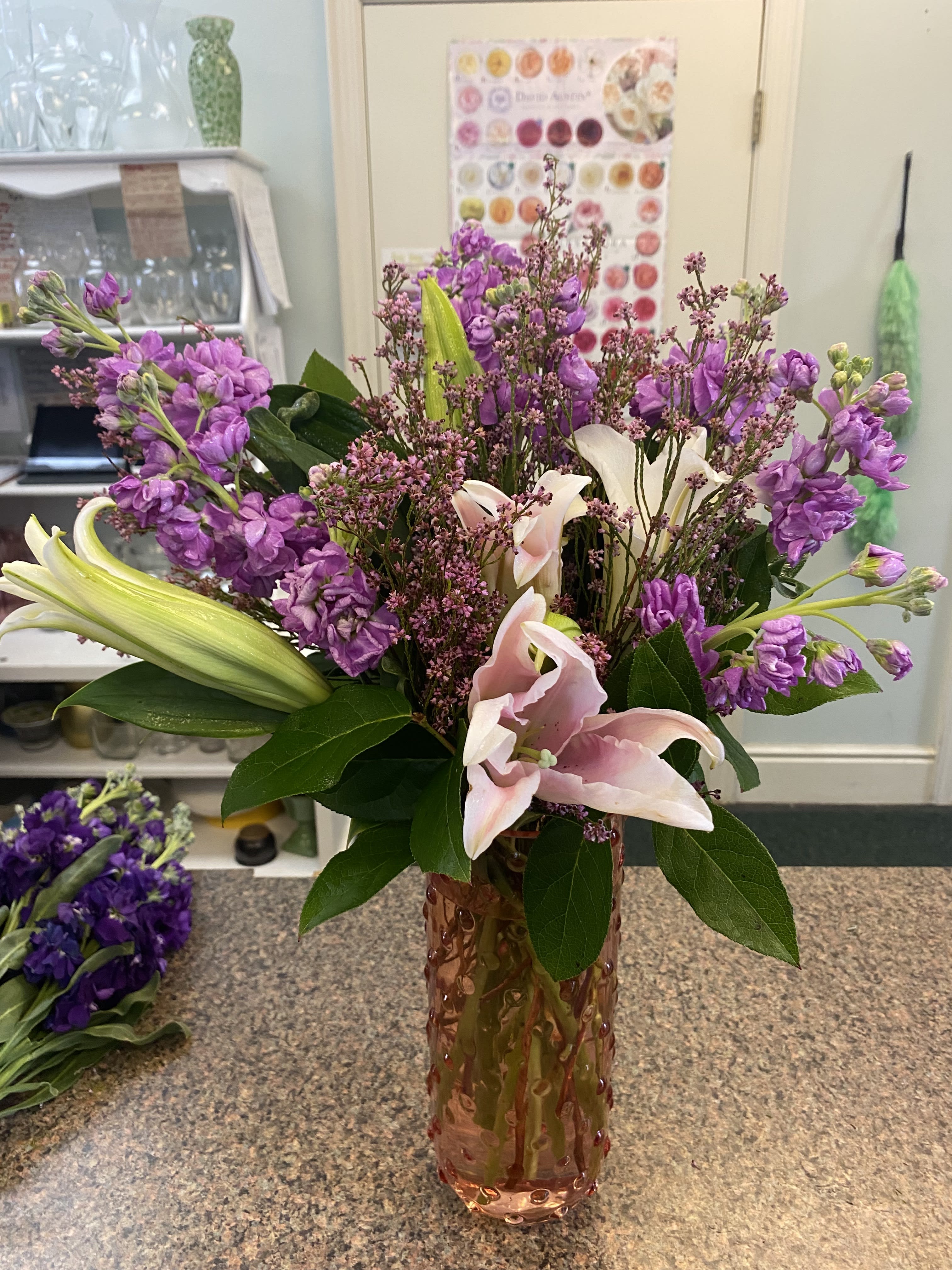 Pink lilies and purple flowers arranged in a tall glass vase