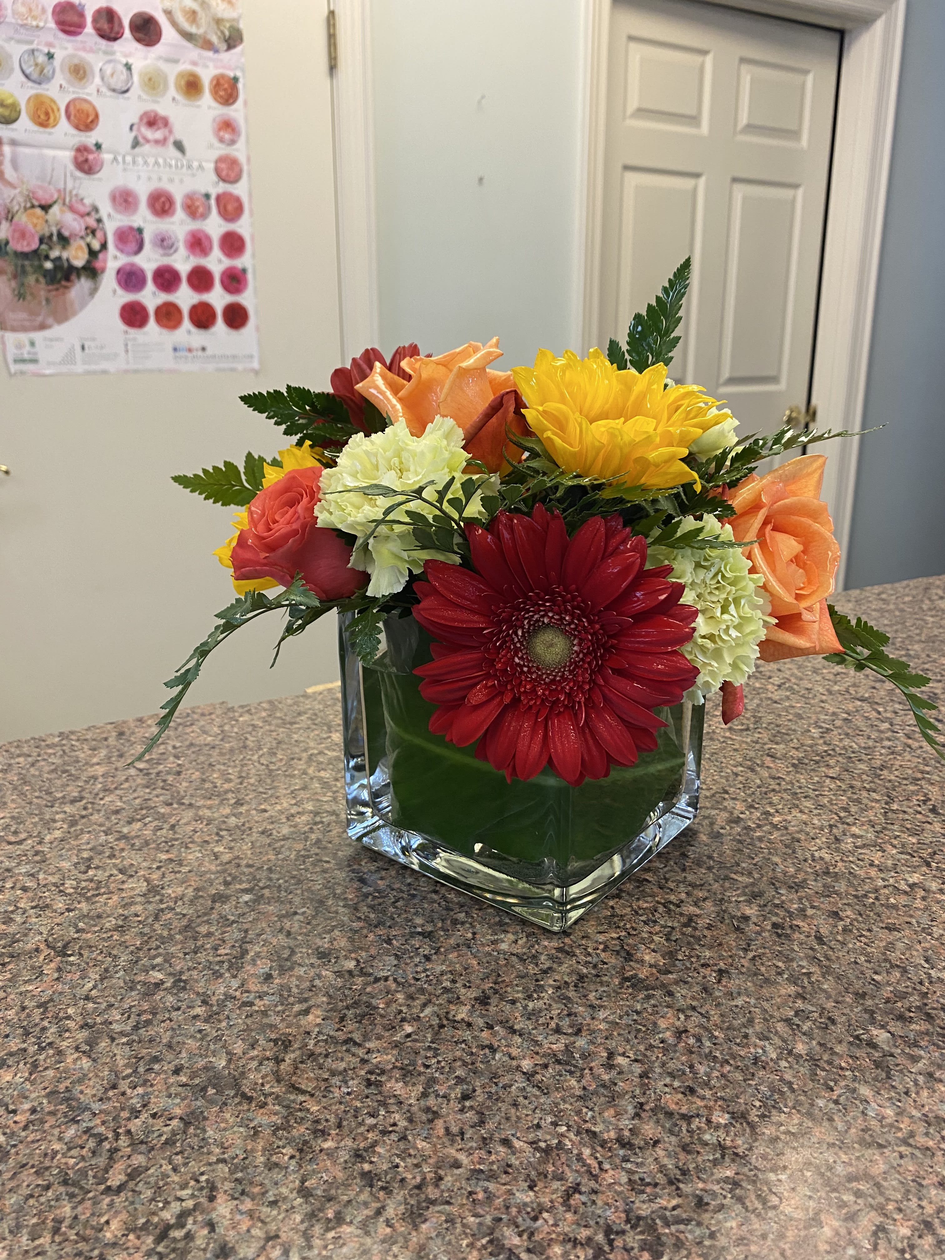 Mixed bouquet in a square glass vase with red, orange, yellow, and pale green blooms
