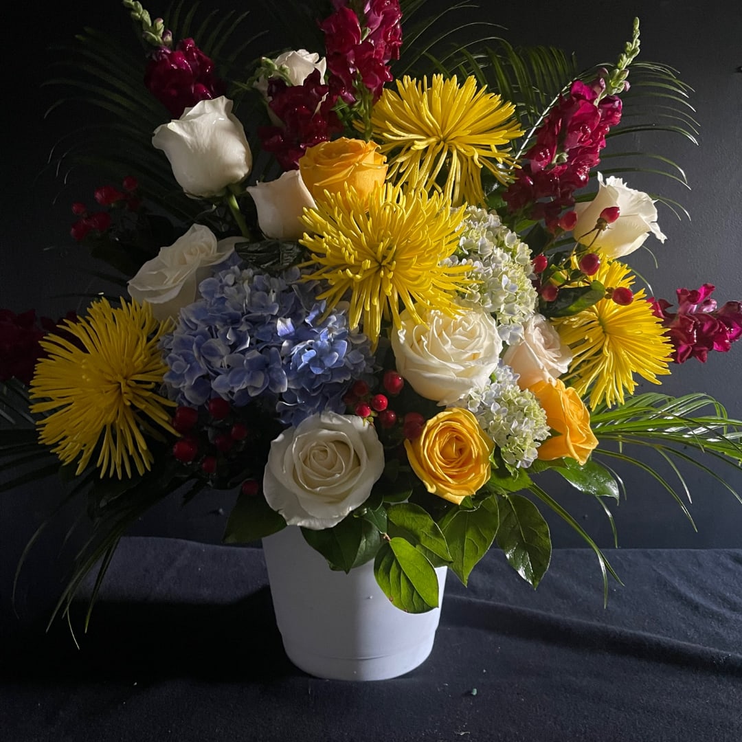 Mixed bouquet of roses, hydrangea, and yellow spider mums in a white vase