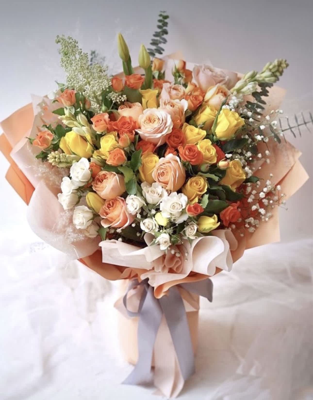 Bouquet of peach, yellow, and white roses wrapped in pastel paper