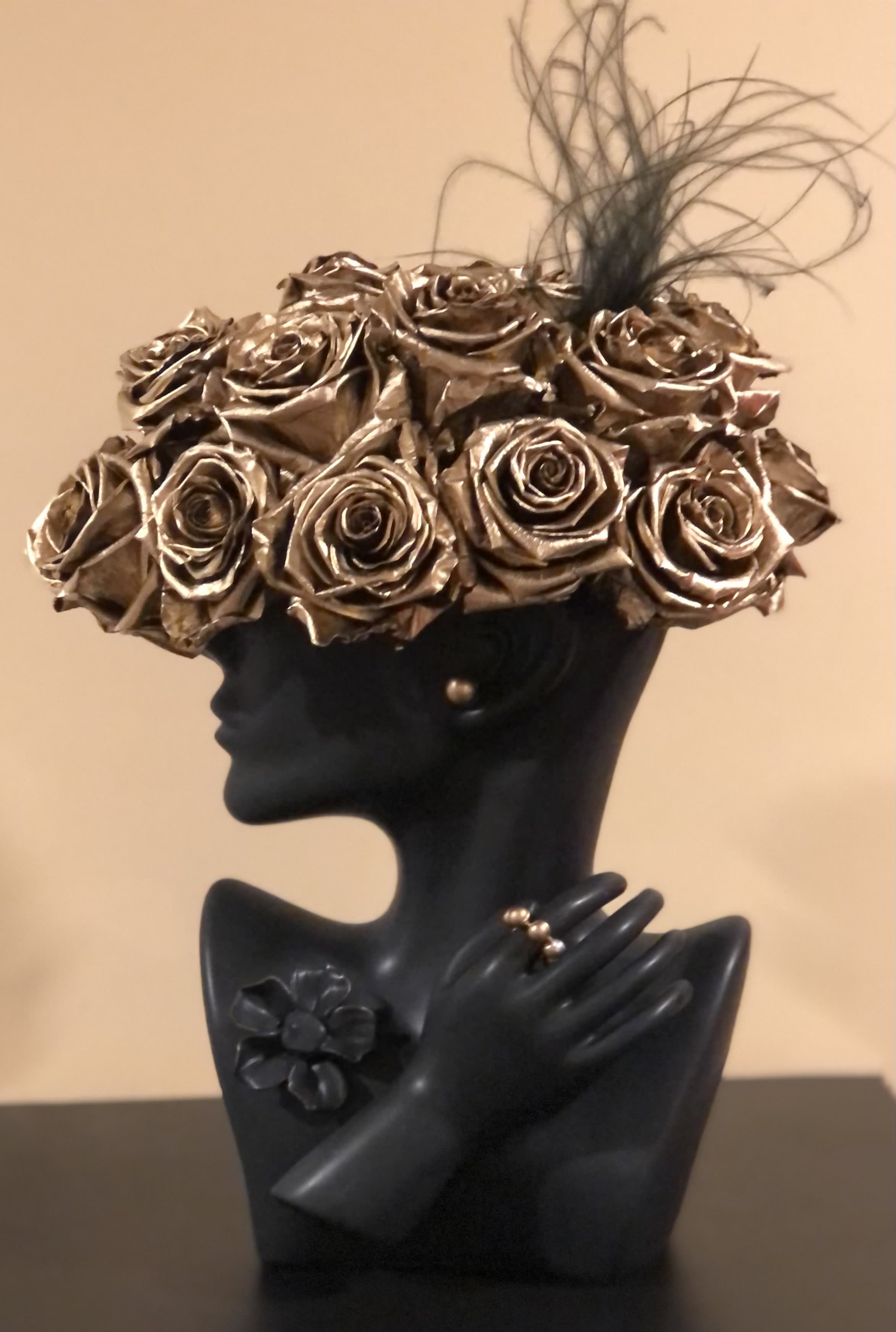 Black bust sculpture topped with metallic gold roses and feather accents